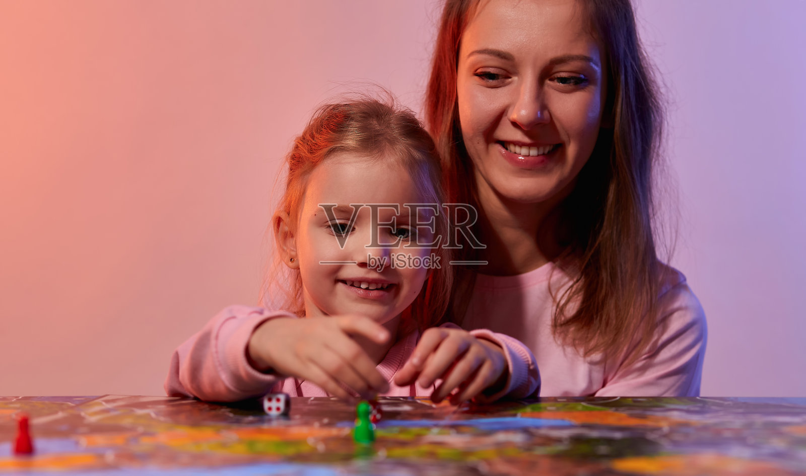 一家人在家里一起玩棋盘游戏玩得很开心。棋盘游戏领域，许多数字，硬币和沙漏。妈妈和可爱的小女儿玩着，手里拿着卡片，脸上洋溢着喜悦的情绪。照片摄影图片