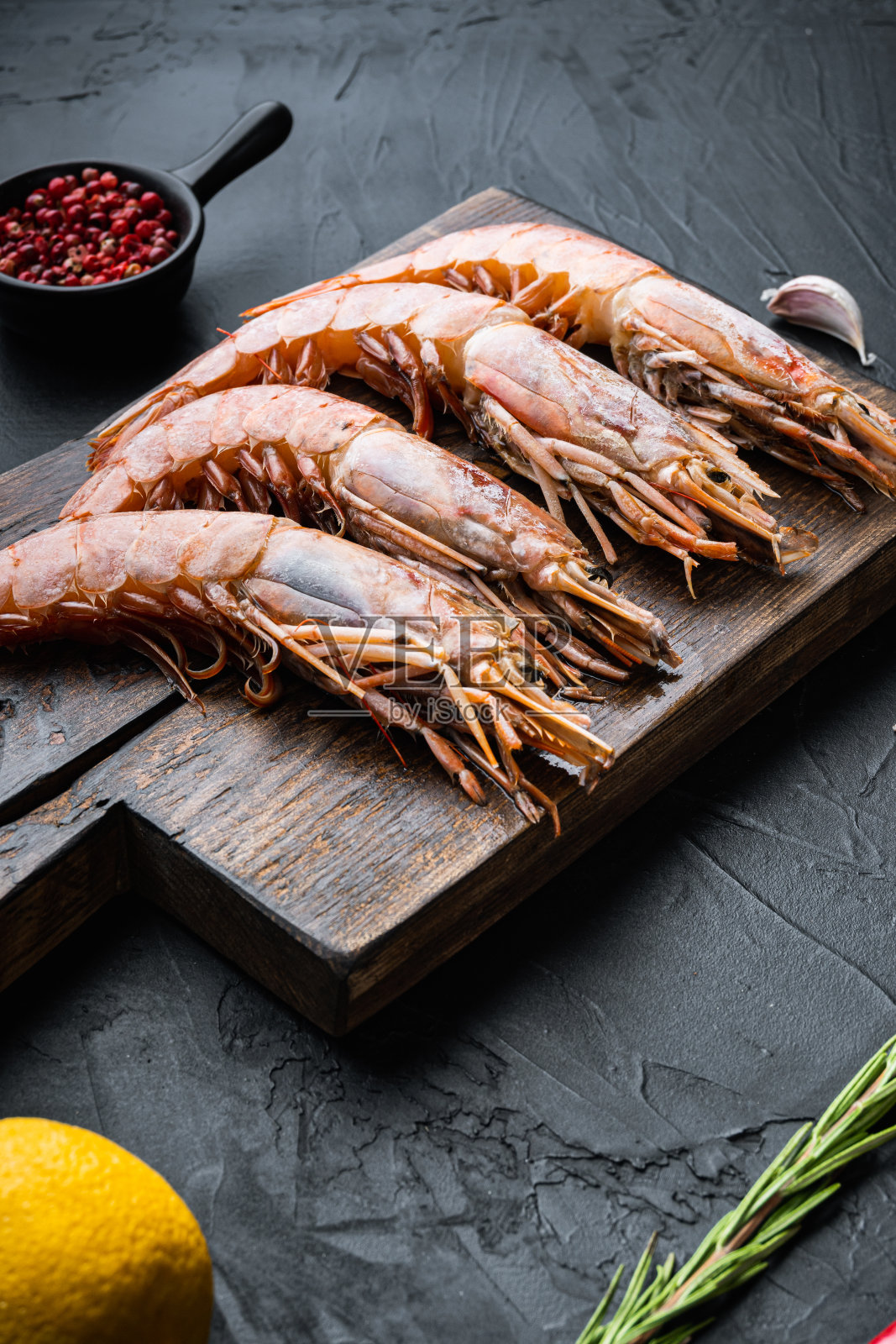 海鲜虾放在木砧板上，配上香料、胡椒和柠檬，放在黑色的混凝土表面照片摄影图片
