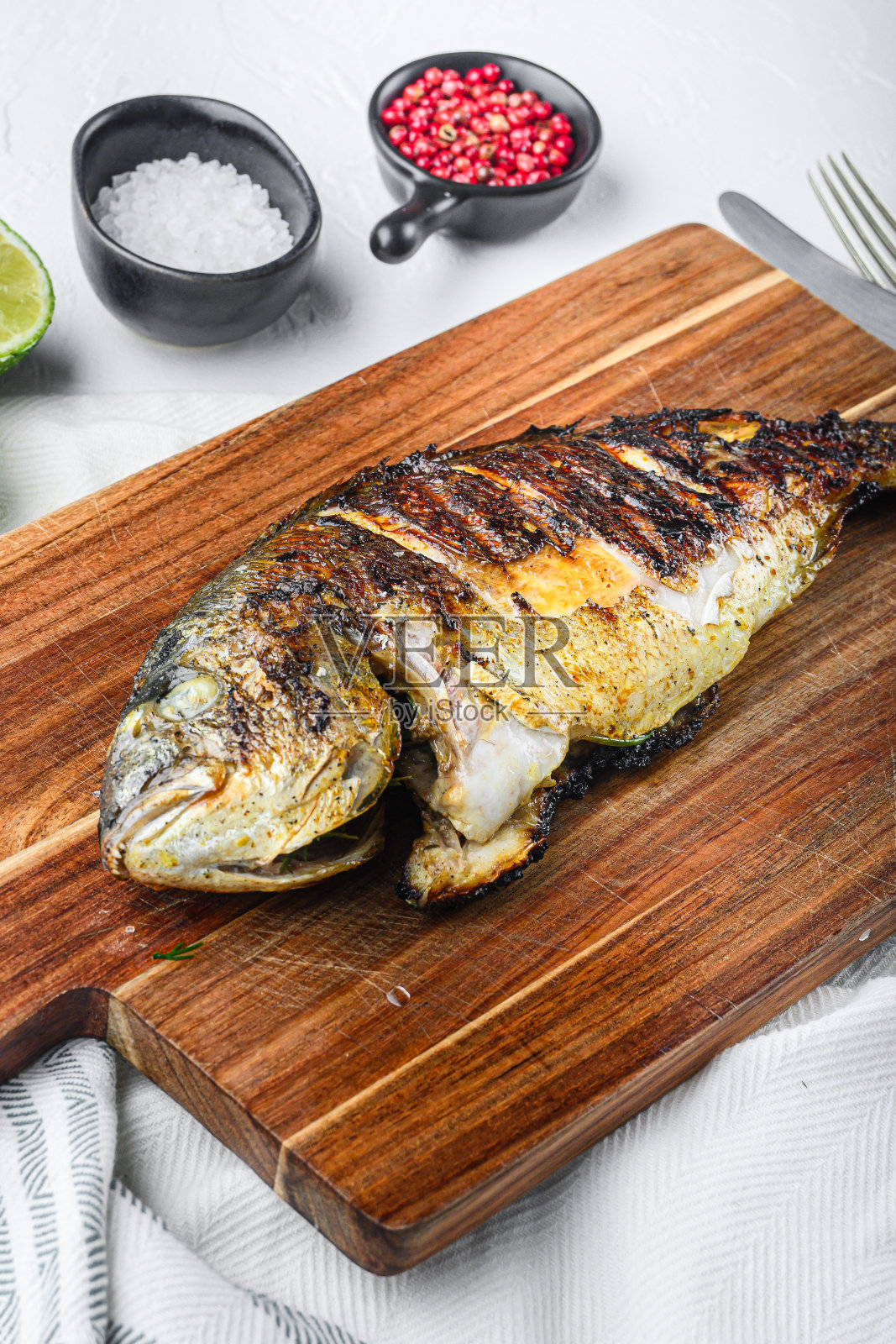 烤鲷鱼或多拉多生鱼，配料置于白色纹理背景的砧板上，侧视竖版照片摄影图片