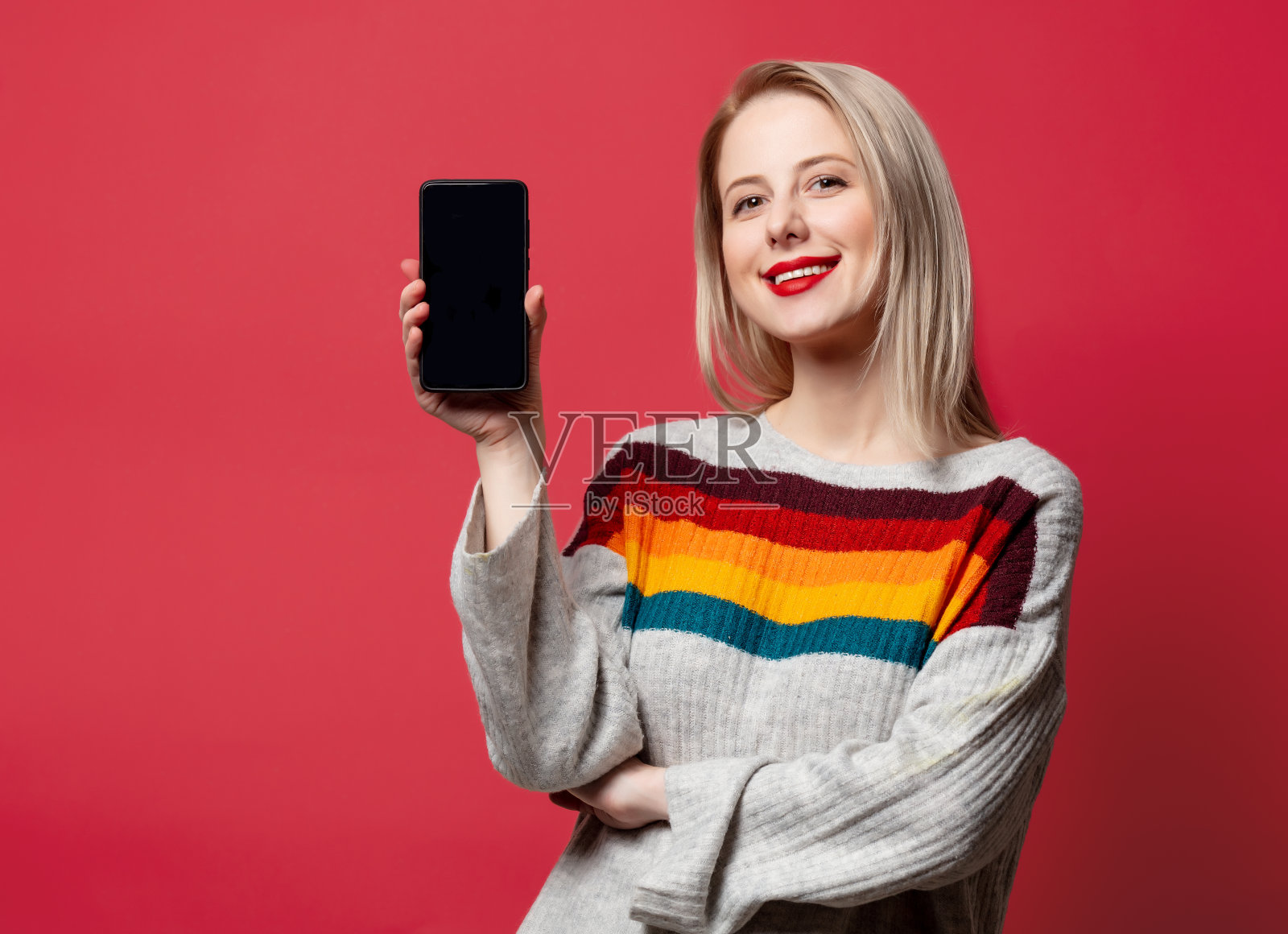 漂亮的金发在毛衣和手机在红色的背景照片摄影图片