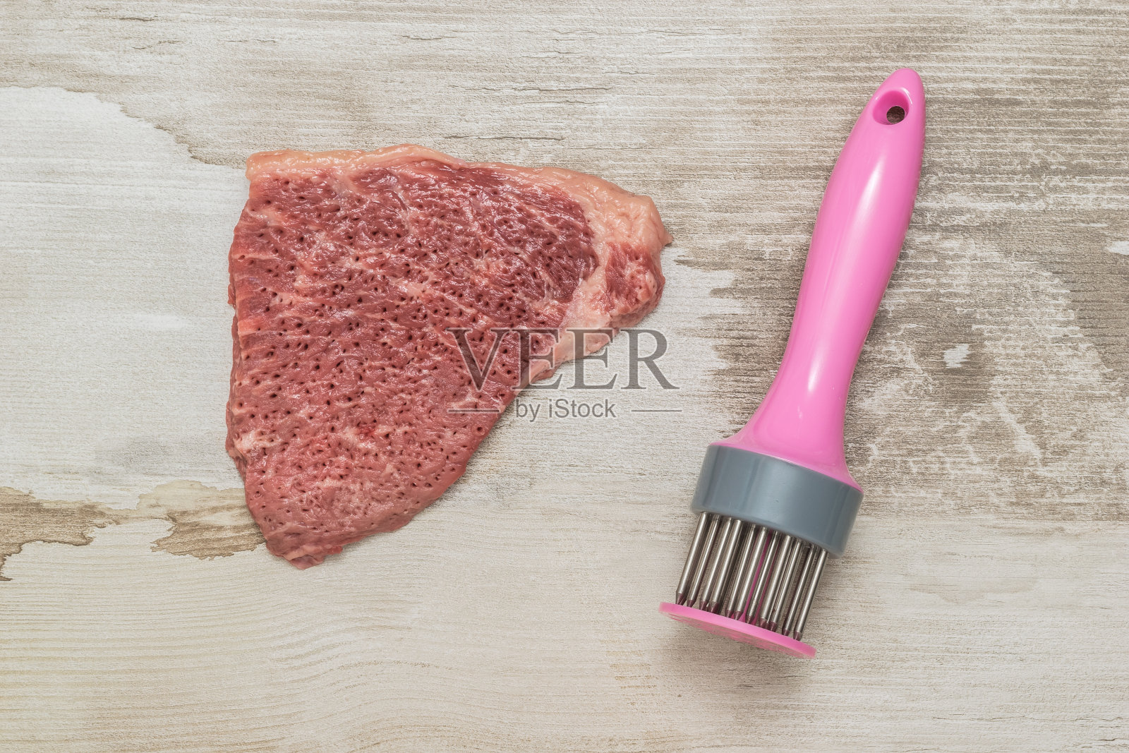 一大块牛肉和一个在木质背景上捣碎肉的装置。照片摄影图片