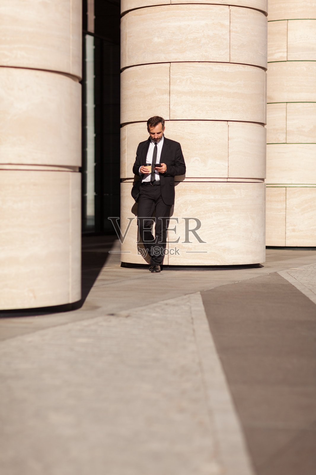 中年商人，手拿外卖咖啡杯，靠在外面的柱子上看手机或看短信照片摄影图片