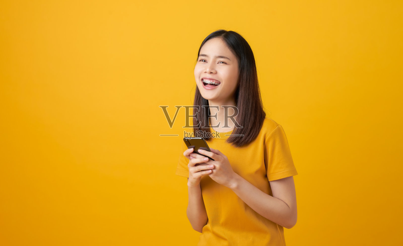 快乐美丽的亚洲女人拿着智能手机在淡黄色的背景。照片摄影图片