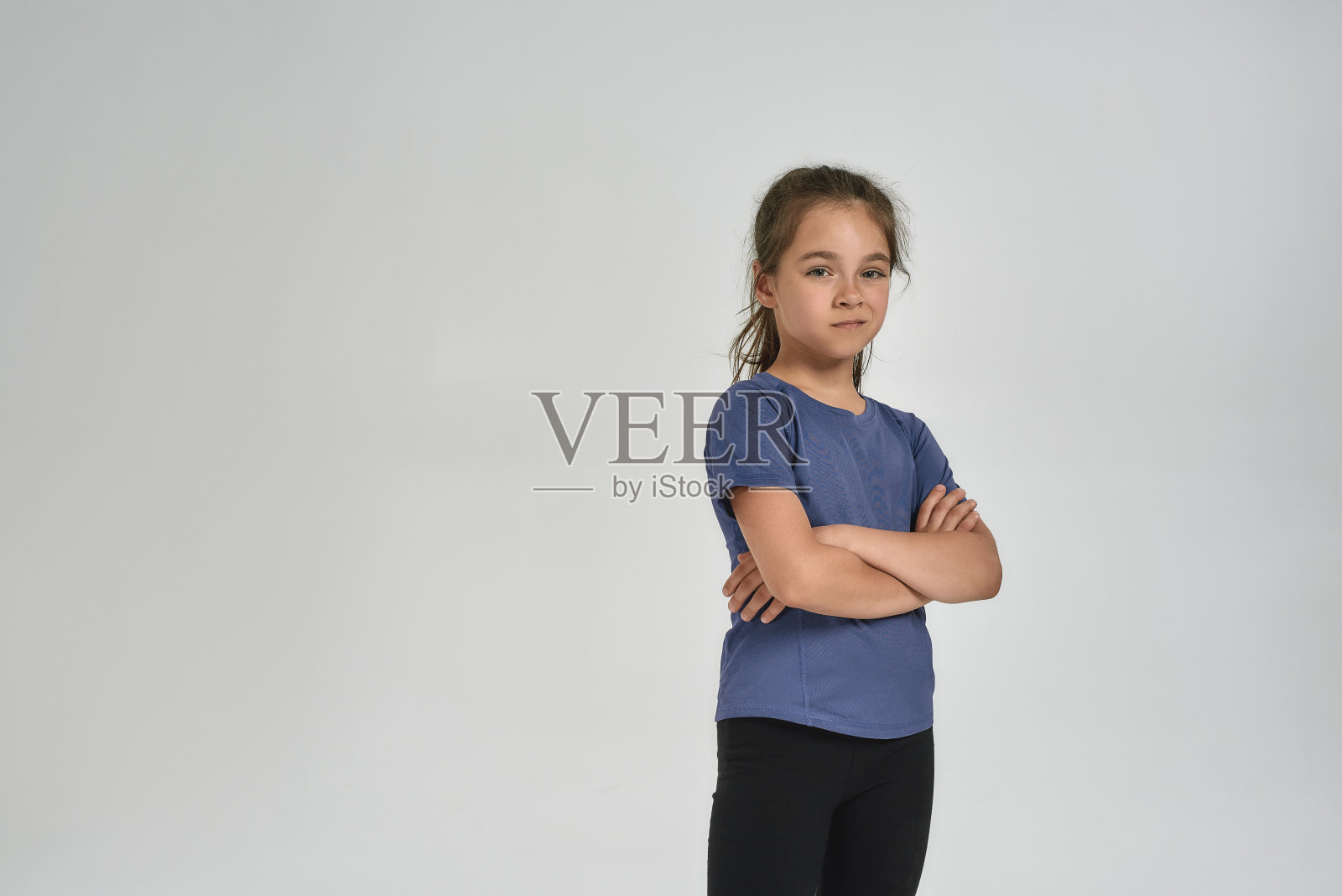 小运动的女孩在运动服看相机，而站着双臂交叉孤立在白色的背景照片摄影图片