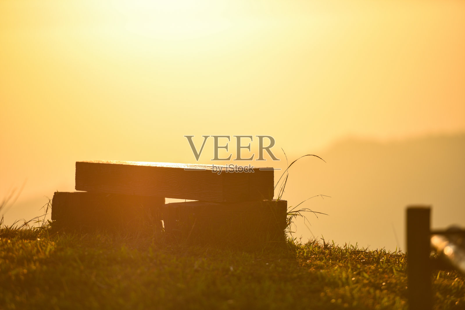 大自然温暖的光线与草地上的木凳，日出或日落在山的背景。照片摄影图片