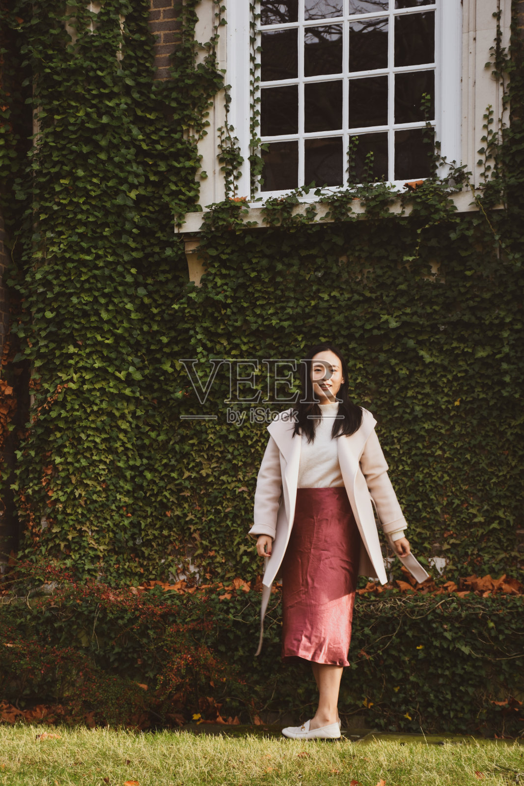 一个女人站在爬满常春藤的美丽墙壁前的肖像。照片摄影图片
