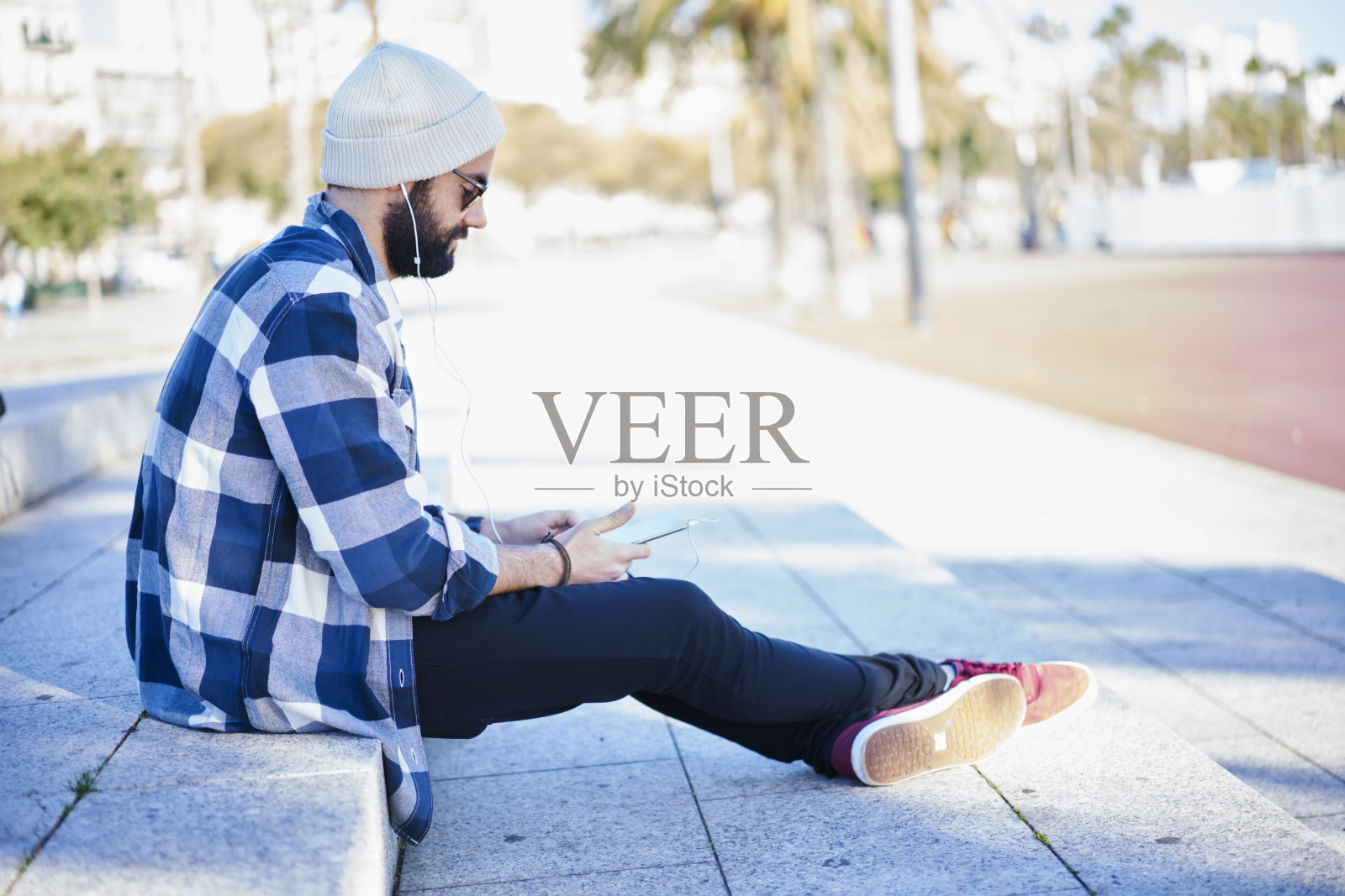 年轻的时尚男子听音乐耳机，而坐在街上照片摄影图片