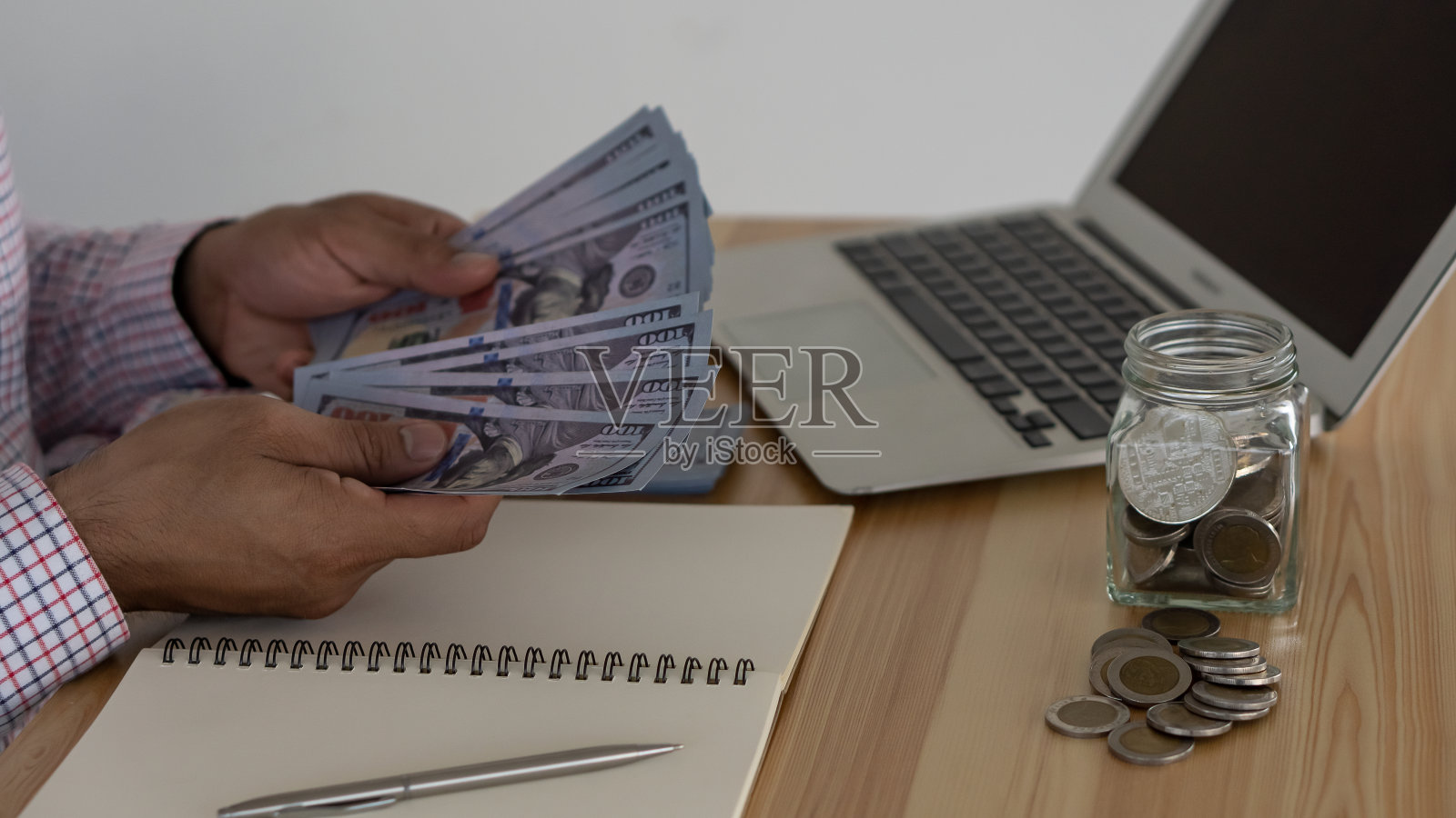 一个商人手里拿着一美元，桌上放着一个笔记本和一瓶硬币照片摄影图片
