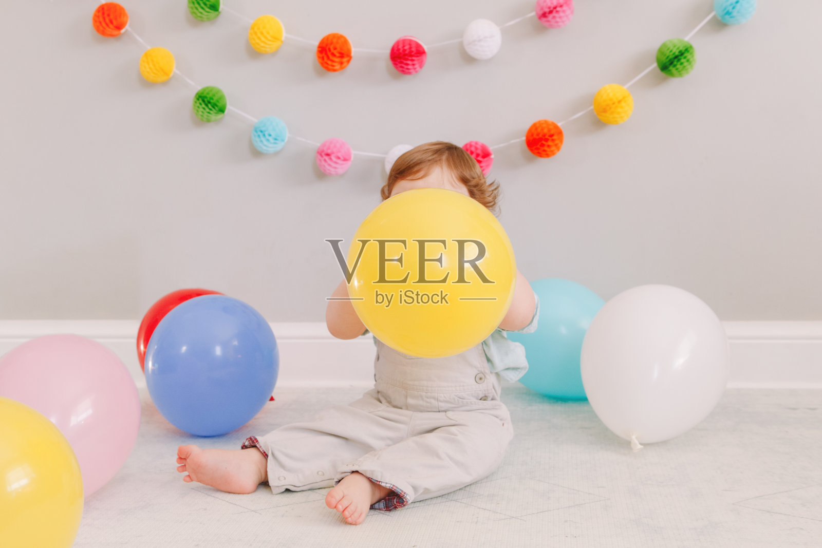 有趣的白人小男孩庆祝一岁生日。小孩子坐在地板上，手里拿着彩色气球。在家庆祝活动或聚会。生日快乐生活理念。照片摄影图片