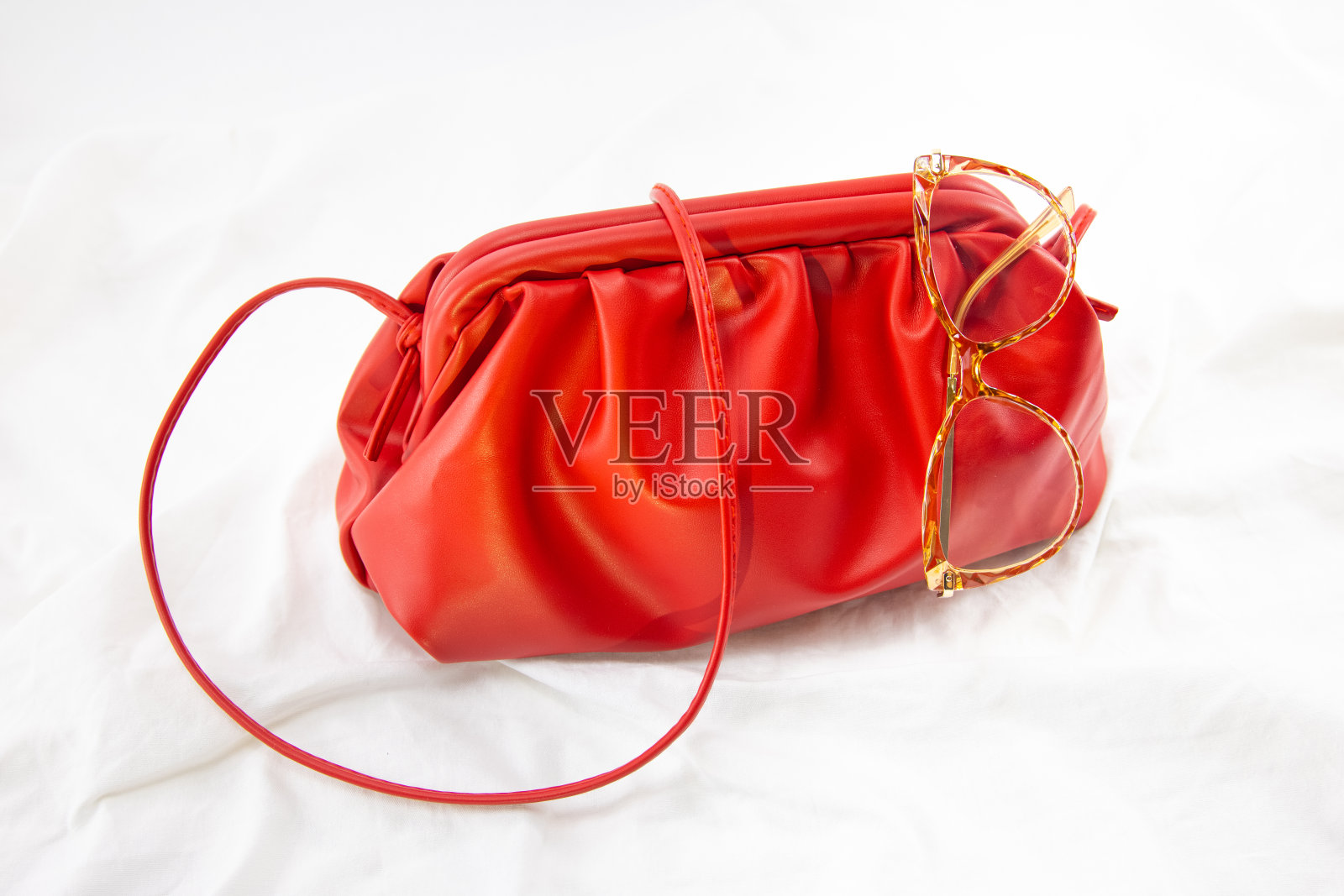 女士手提包与黑色太阳镜在一个白色的背景。皮包上有褶皱织物。侧视图时尚概念花哨时尚眼镜和豪华真皮全纹包照片摄影图片