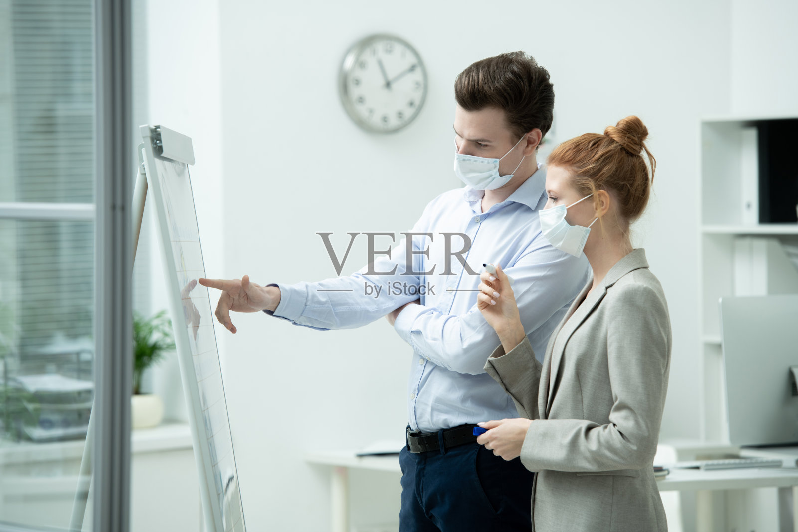 戴着防护面具的年轻男性经理指着白板上的数据照片摄影图片