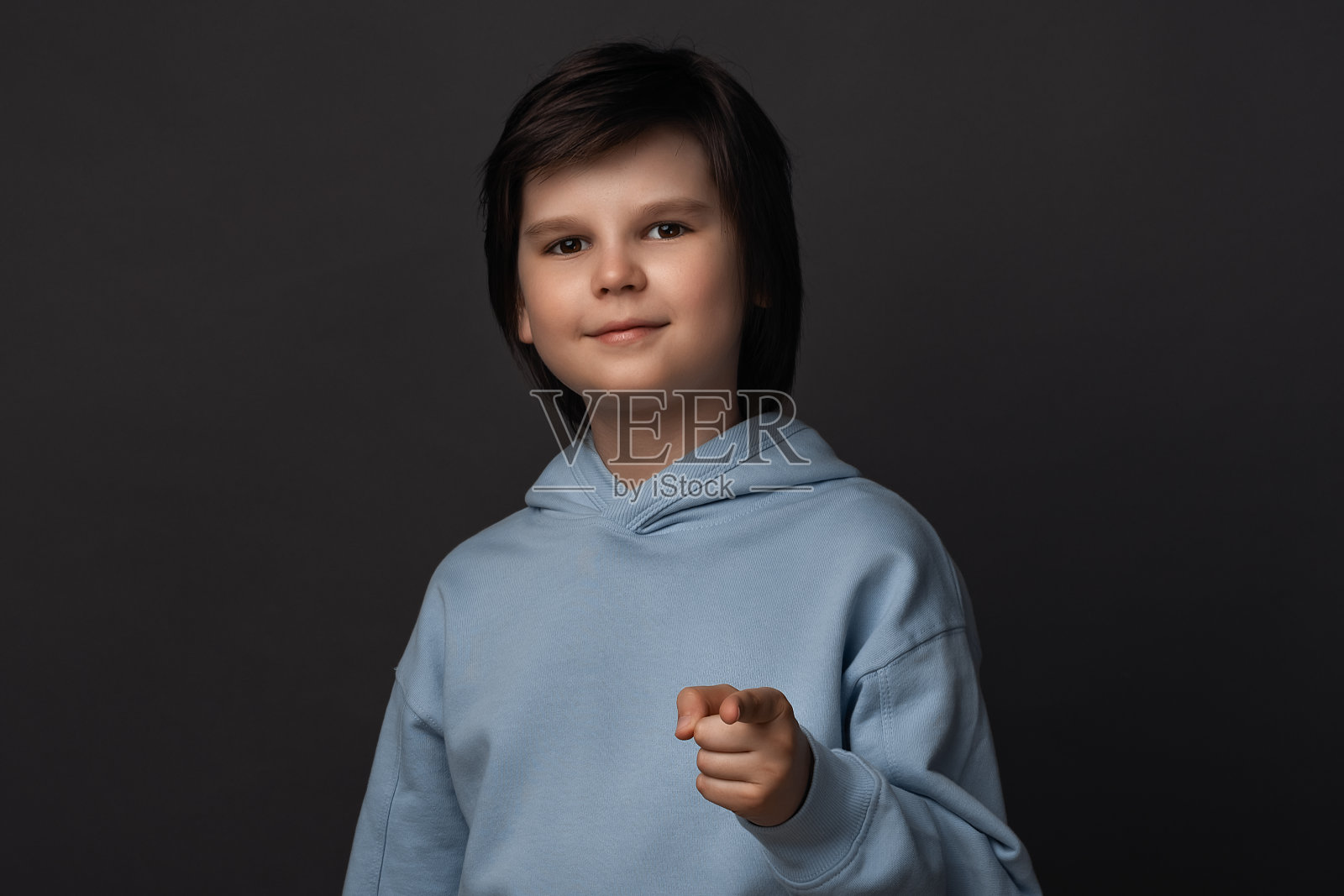 10-12岁的可爱男孩看着镜头，用手指着你。工作室拍摄，灰色背景照片摄影图片