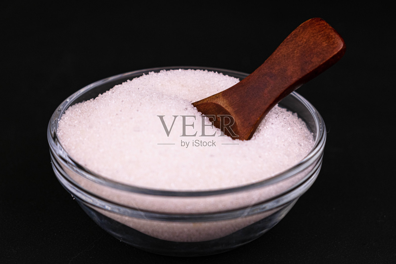 糖在一个玻璃碗和一个木勺在黑色的背景。特写镜头。照片摄影图片