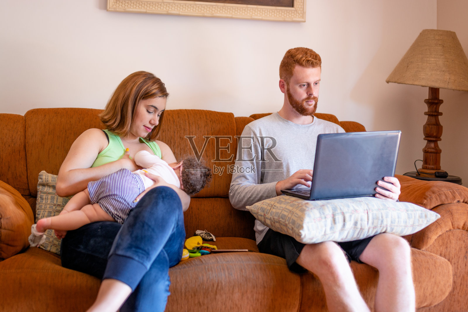 一家人坐在沙发上，用笔记本电脑工作，和婴儿玩照片摄影图片