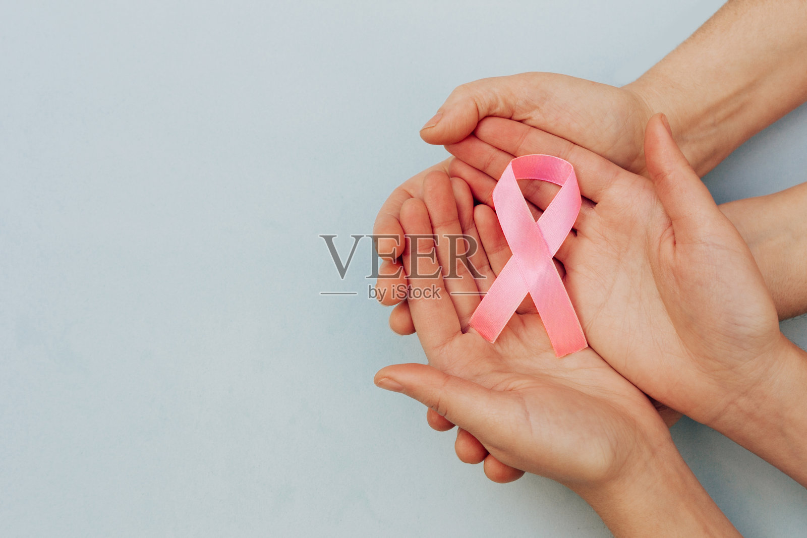照片的粉红色丝带，象征着癌症，在女人的手上和一个蓝色的背景与复印空间在左边照片摄影图片