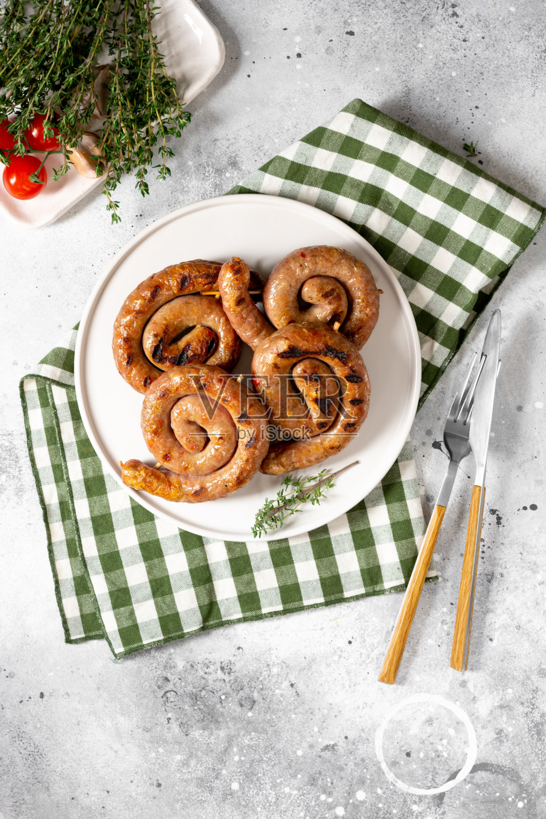 浅灰色的桌子上的餐盘上螺旋状的煎香肠。螺旋香肠。自制肉炒香肠照片摄影图片