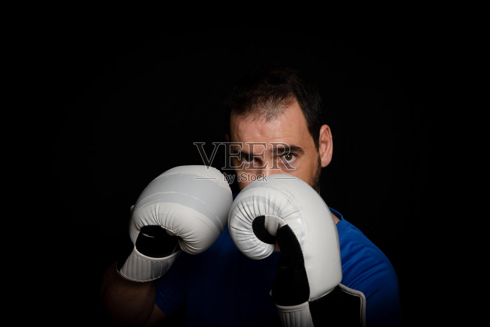 身穿蓝色t恤和拳击手套的大胡子男子在黑色背景下摆姿势照片摄影图片