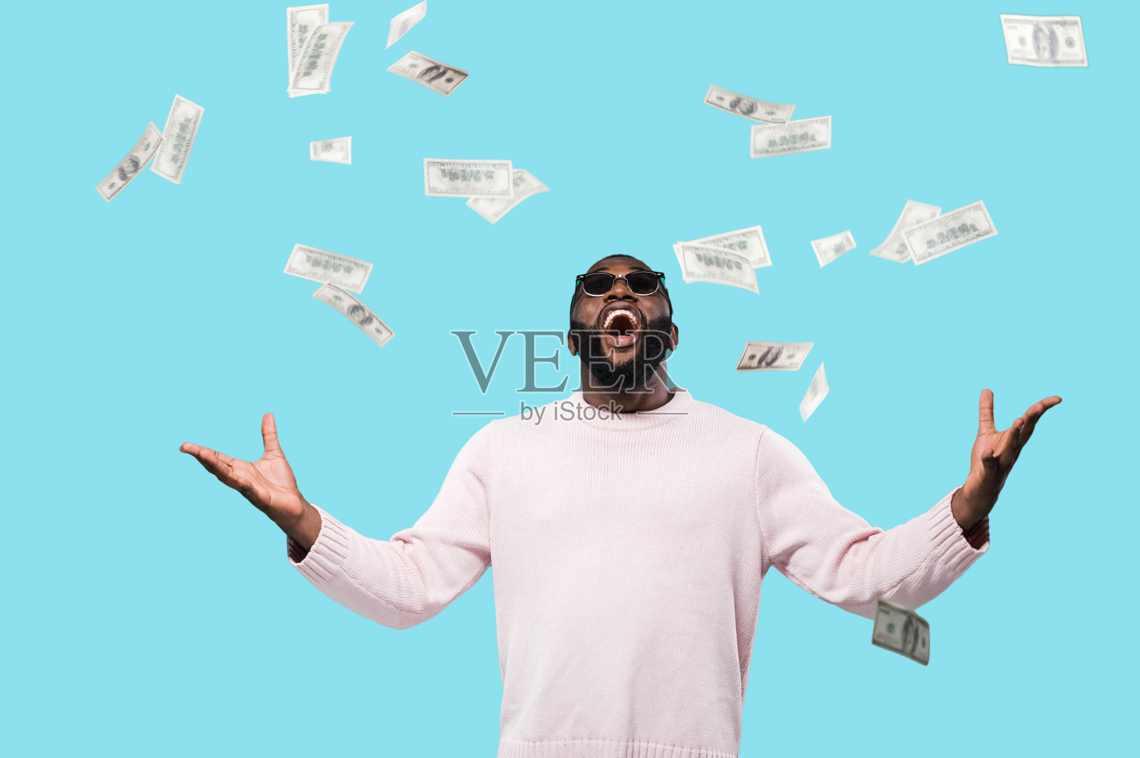快乐快乐尖叫的非洲裔美国人戴着太阳镜抬头看掉落的钱，中奖的彩票站在孤立的蓝色背景照片摄影图片