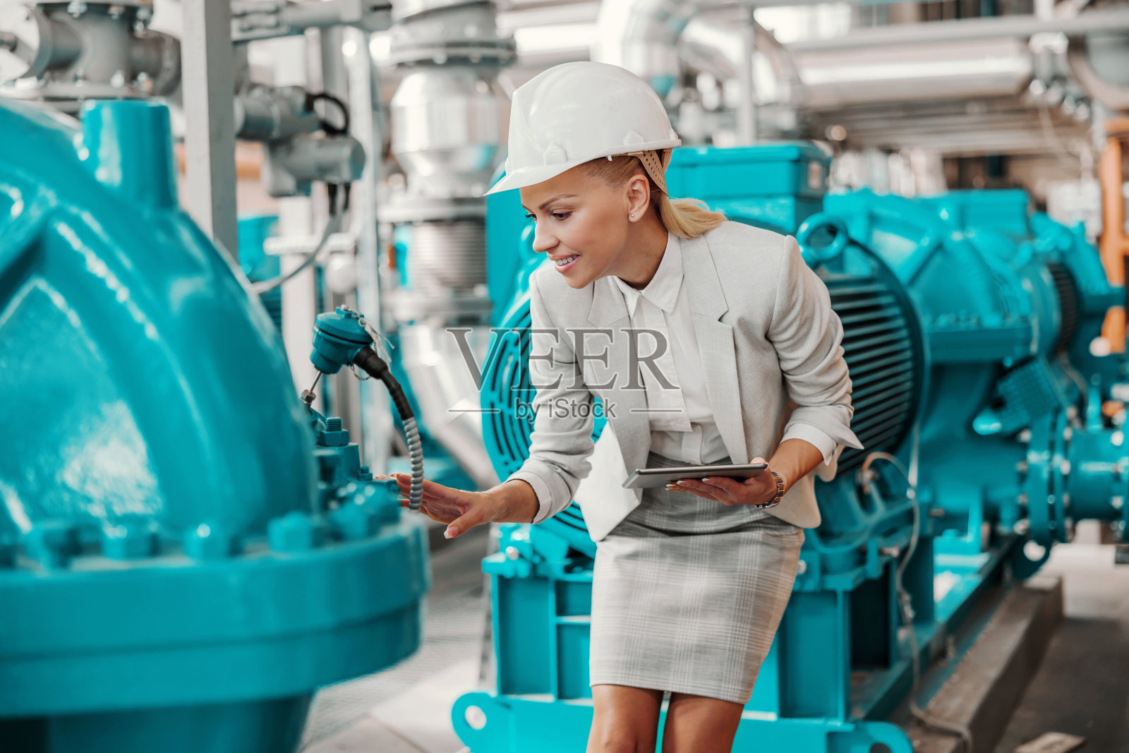 成功微笑，努力工作的女经理穿着西装站在加热厂，手里拿着平板检查涡轮机。照片摄影图片