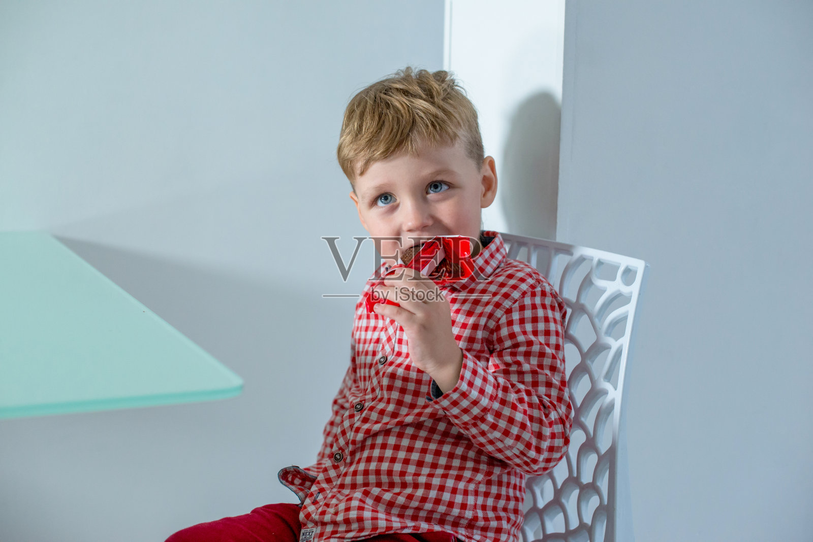 男孩坐在厨房里，坐在桌子上吃糖果。照片摄影图片