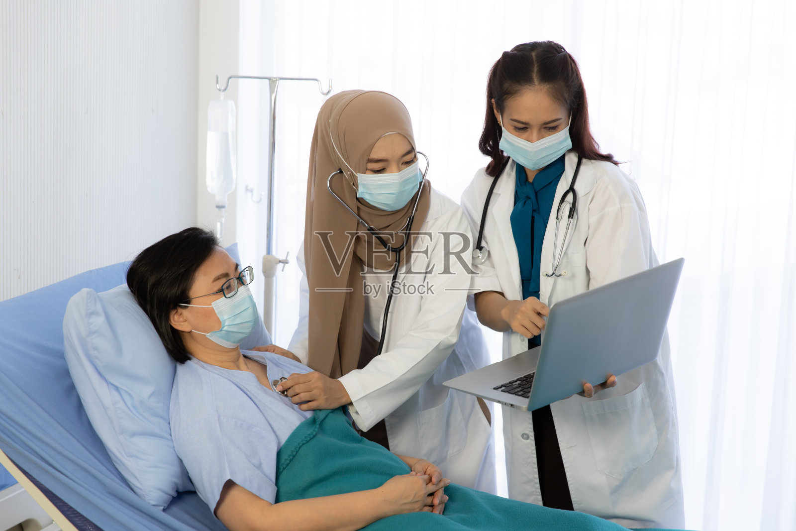 年轻的亚洲妇女穆斯林医生和协助检查老人坐在病床上的医院。医疗卫生安全与Covid-19康复理念照片摄影图片