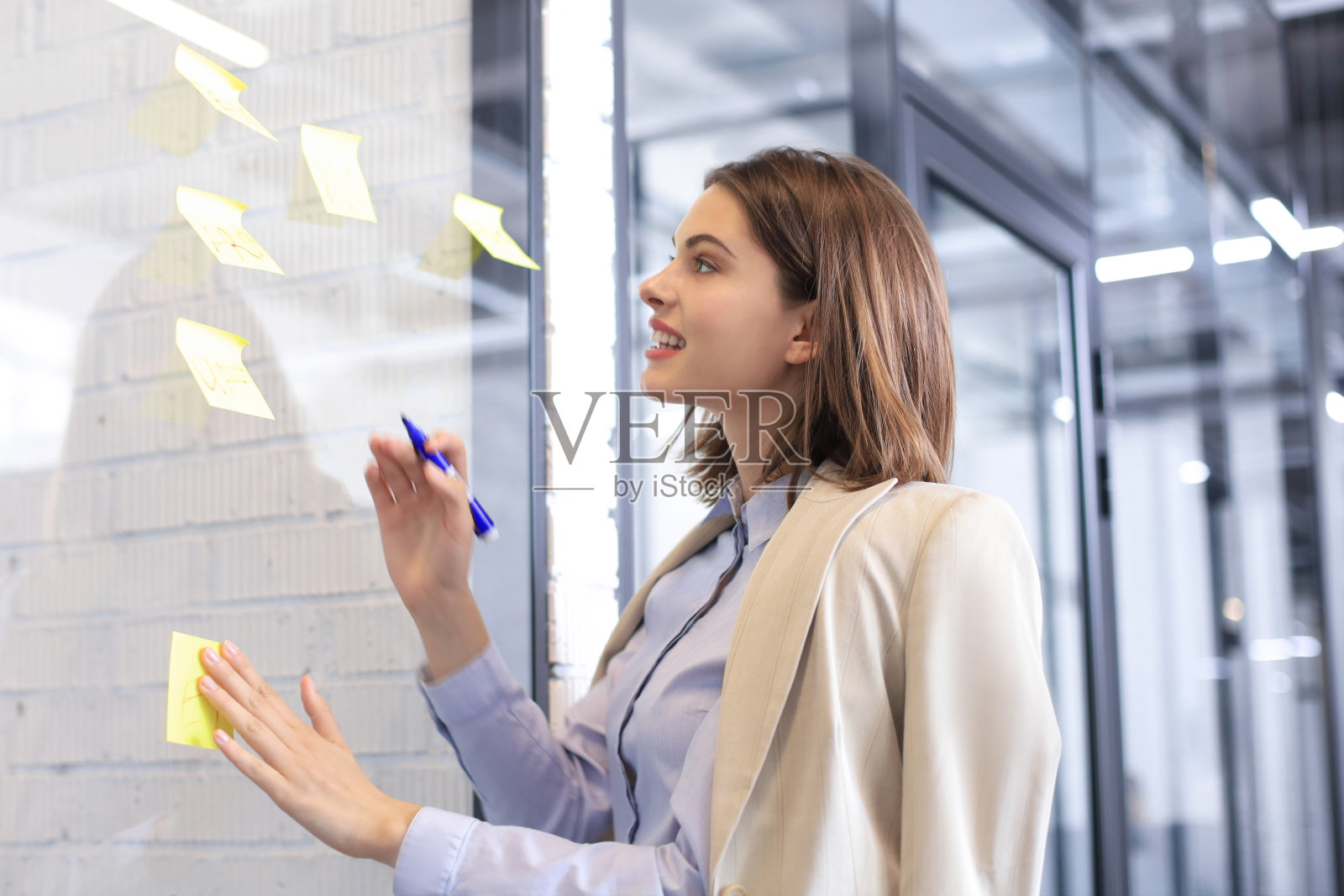 迷人的女商人贴在办公室的玻璃上并在上面写字。照片摄影图片