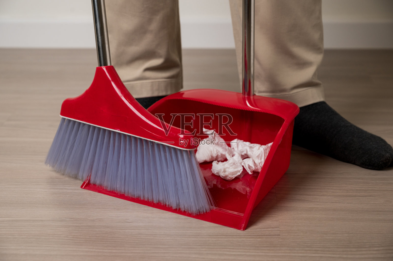 近处，年轻人拿着簸箕，用红扫把清扫房子地板上的纸垃圾。家庭清洁设备红色。照片摄影图片