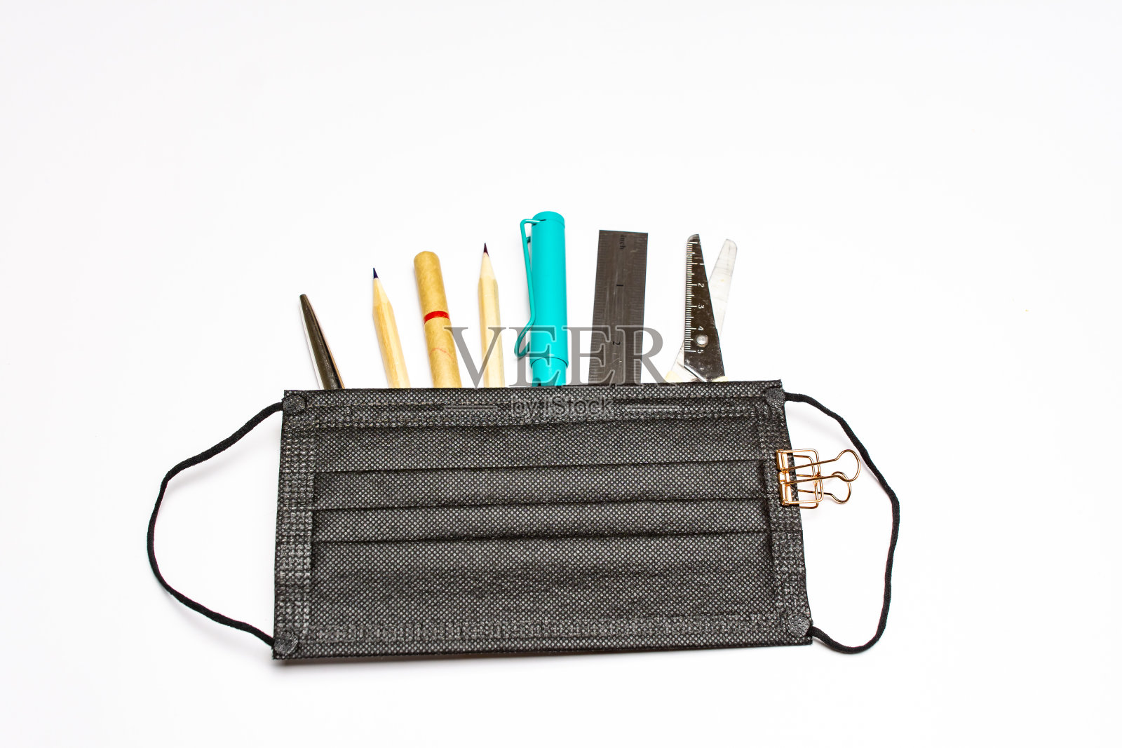 一个黑色医用口罩躺在白色背景下，口罩下面平躺着各种文具用品。前视图。照片摄影图片