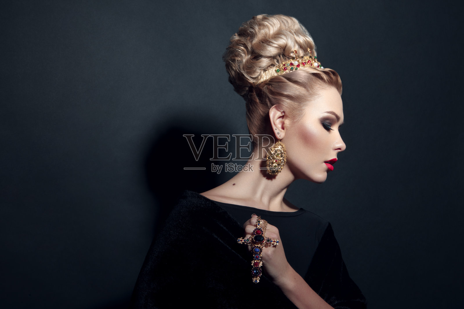 一个金发女孩的特写形象与美发，化妆，手持十字架，在黑色的背景。照片摄影图片