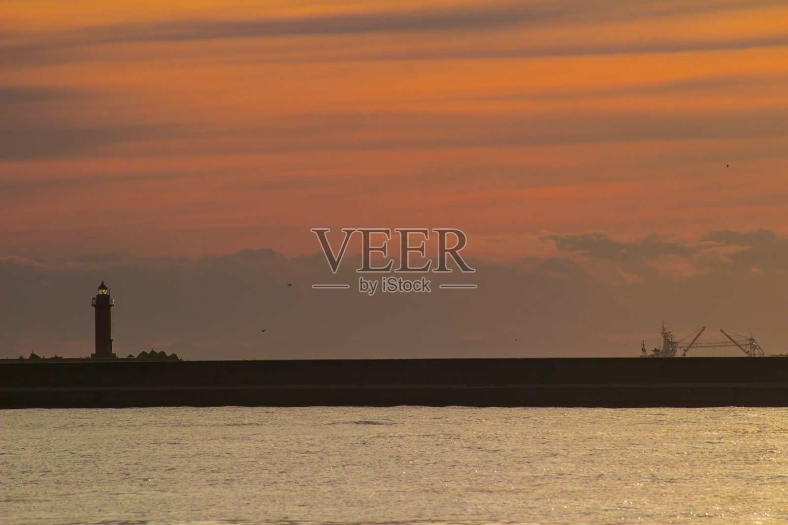 钏路港灯塔的剪影投射在日落时的橙色天空中照片摄影图片