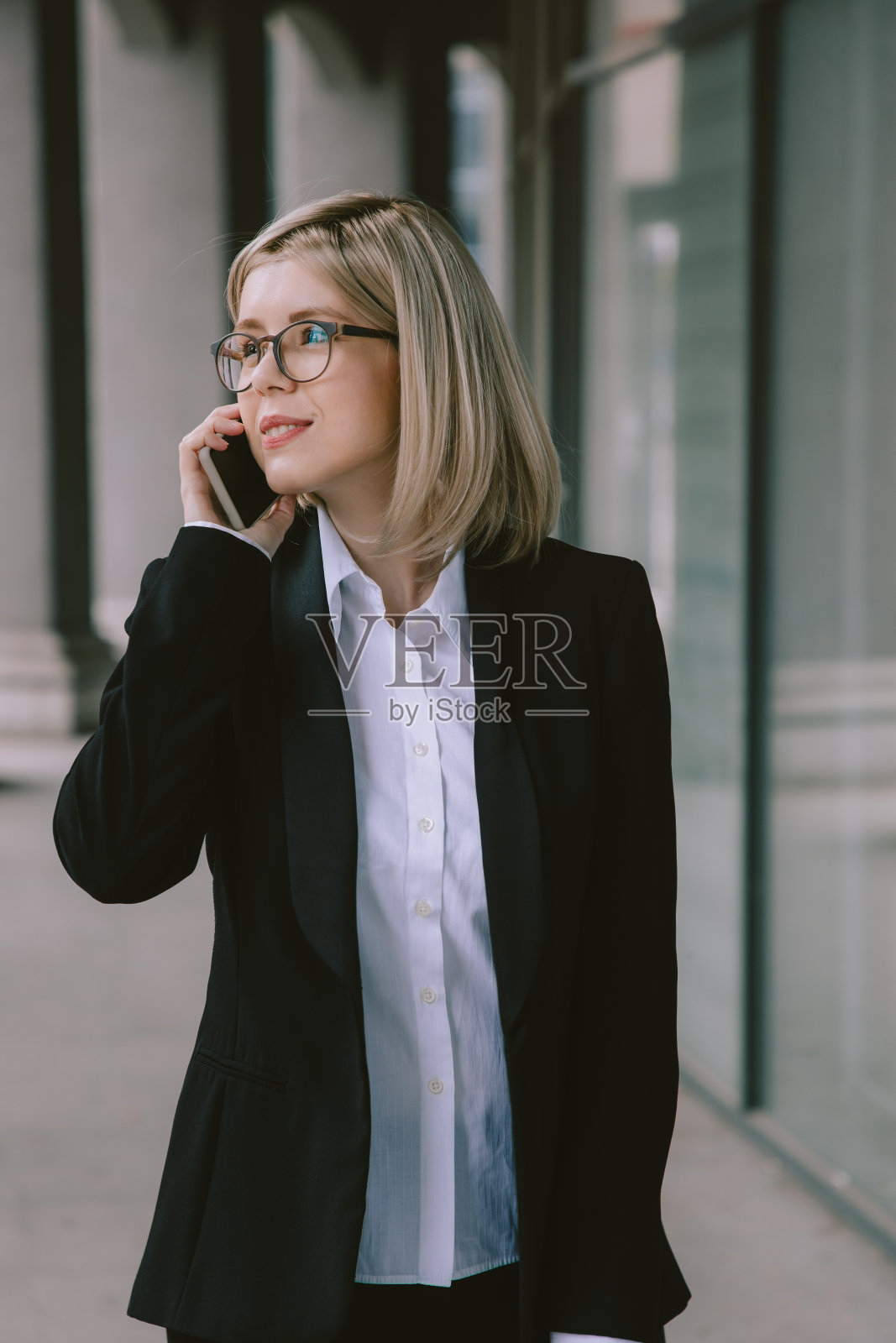 穿着黑色西装的女商人走在城市里，还在用手机照片摄影图片