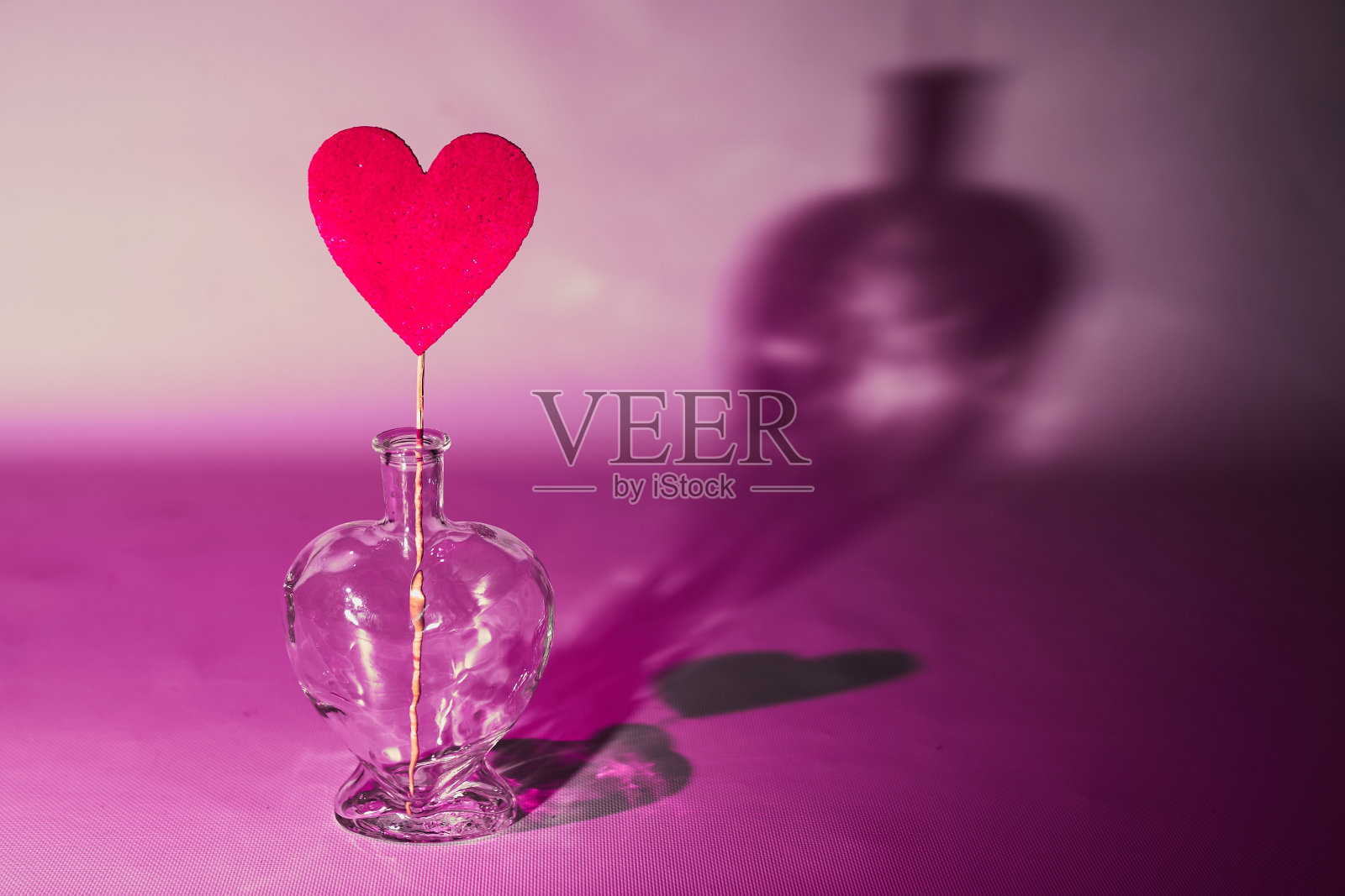 在一个透明的酒瓶里，紫色的卡片上有一个红色的心，背景上有一个坚硬的阴影。照片摄影图片