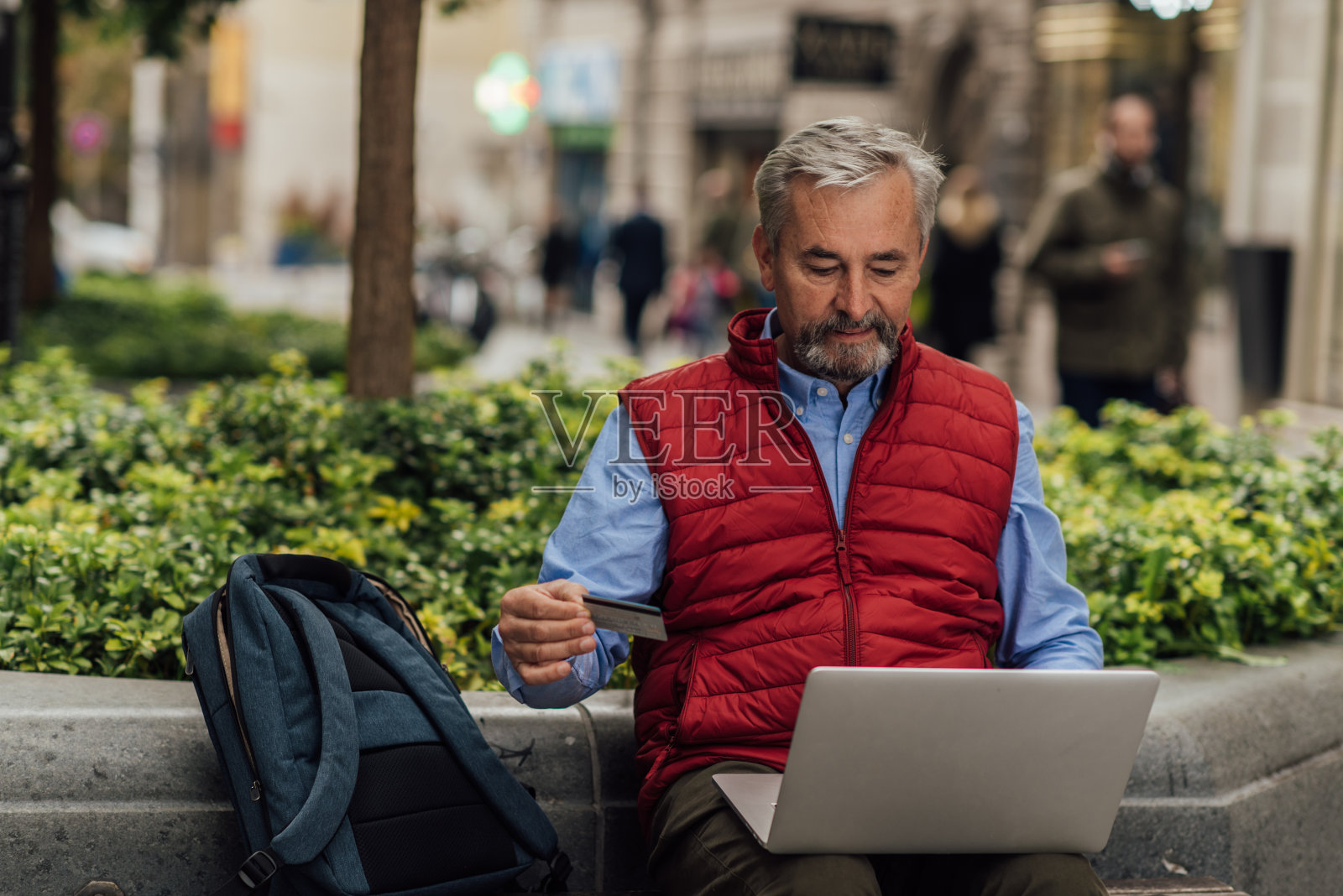 一个老人坐在街上，在他的笔记本电脑上存钱照片摄影图片