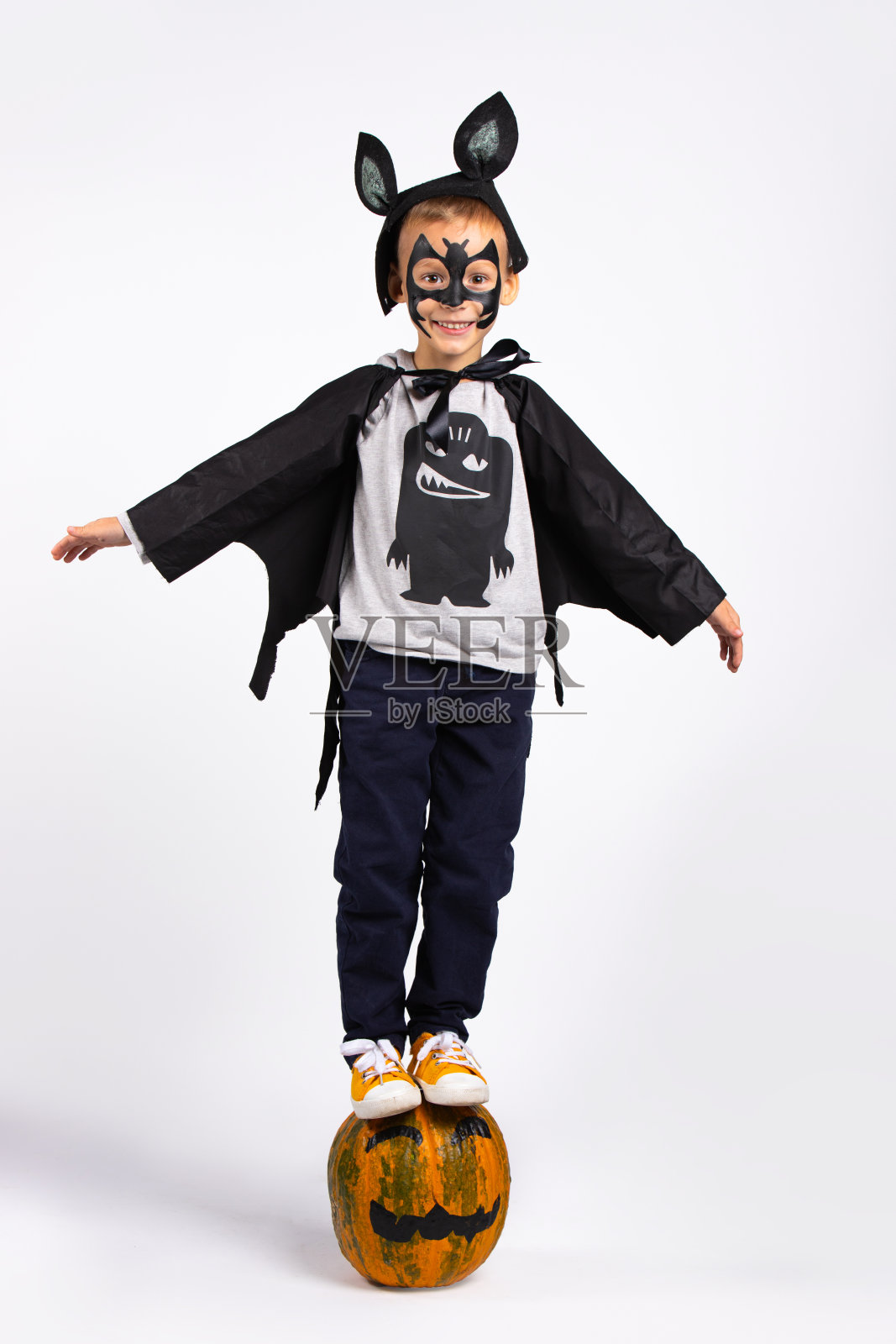 小兴奋的孩子享受着坐在南瓜地里的时光。万圣节儿童化装舞会。穿着万圣节蝙蝠装的男孩坐在南瓜上。有趣的孤立在白色背景和充足的空间照片摄影图片