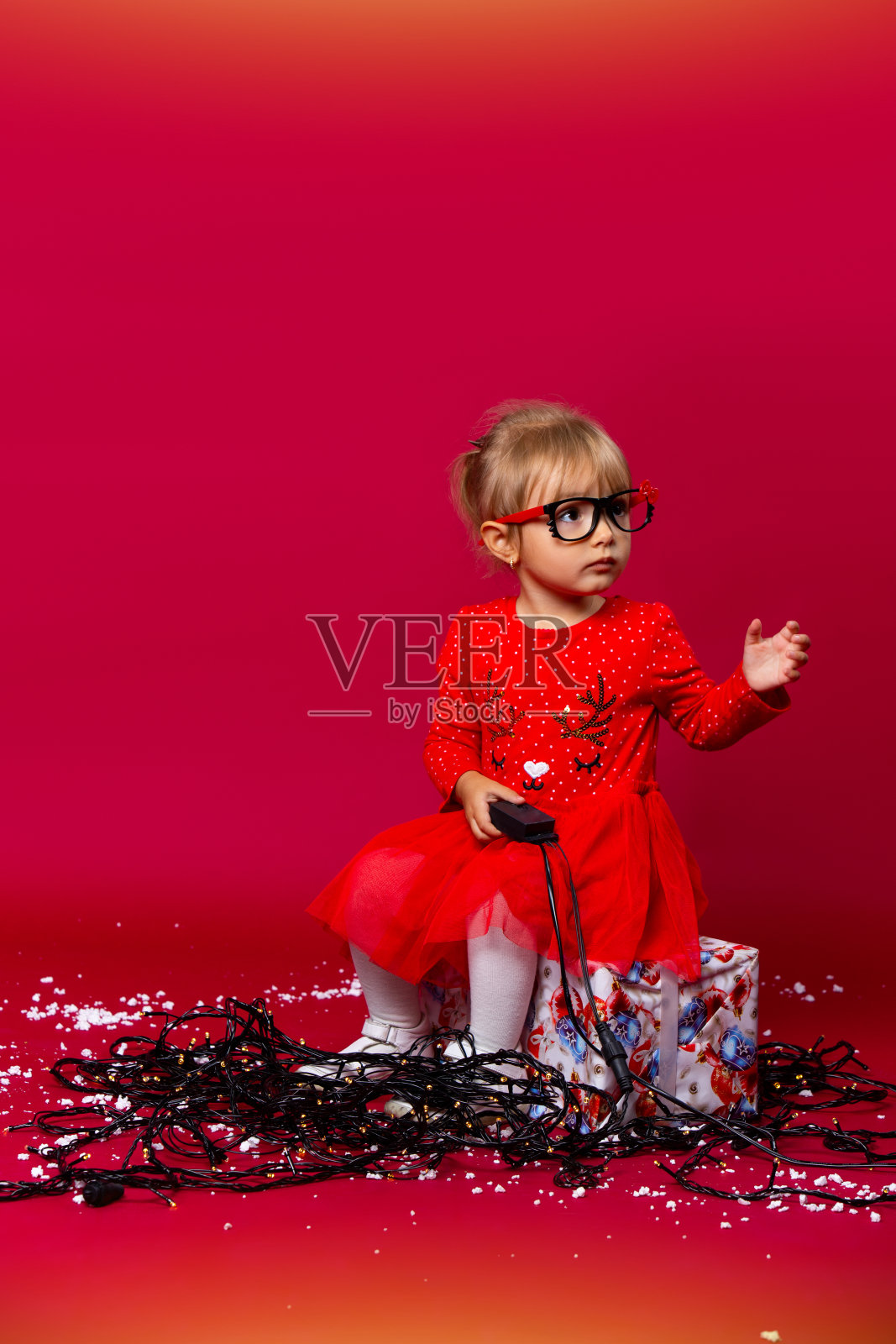 一个小女孩穿着红色的节日服装，戴着新年的花环，在红色的背景上看着旁边，空着空间。照片摄影图片