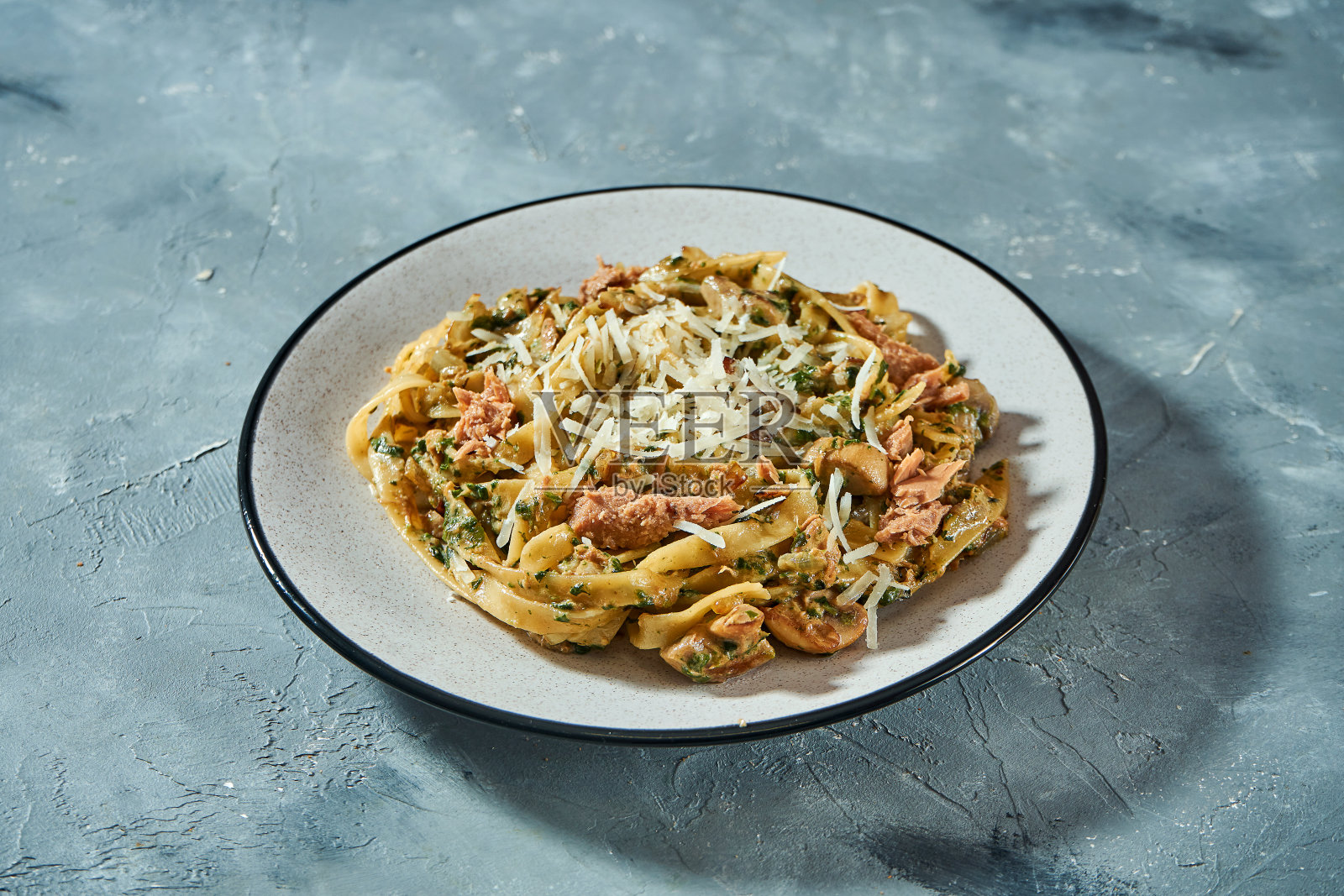 以灰色背景为背景的灰色盘子，配以海鲜、金枪鱼罐头和帕尔马干酪的意大利面食。特写，选择性聚焦照片摄影图片