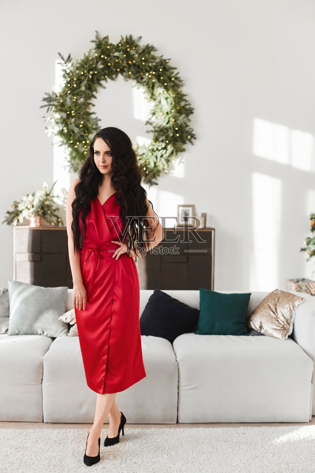 一个年轻的女人穿着红色的晚礼服在客厅内部装饰圣诞节。圣诞快乐，恭贺新禧照片摄影图片