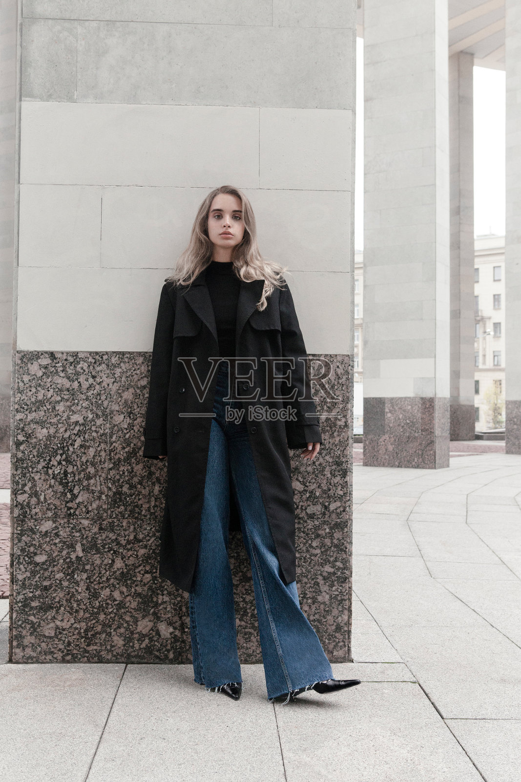 美丽的年轻金发女人自然的化妆穿着黑色外套，高领，高跟鞋和蓝色牛仔裤户外拍摄的城市背景照片摄影图片