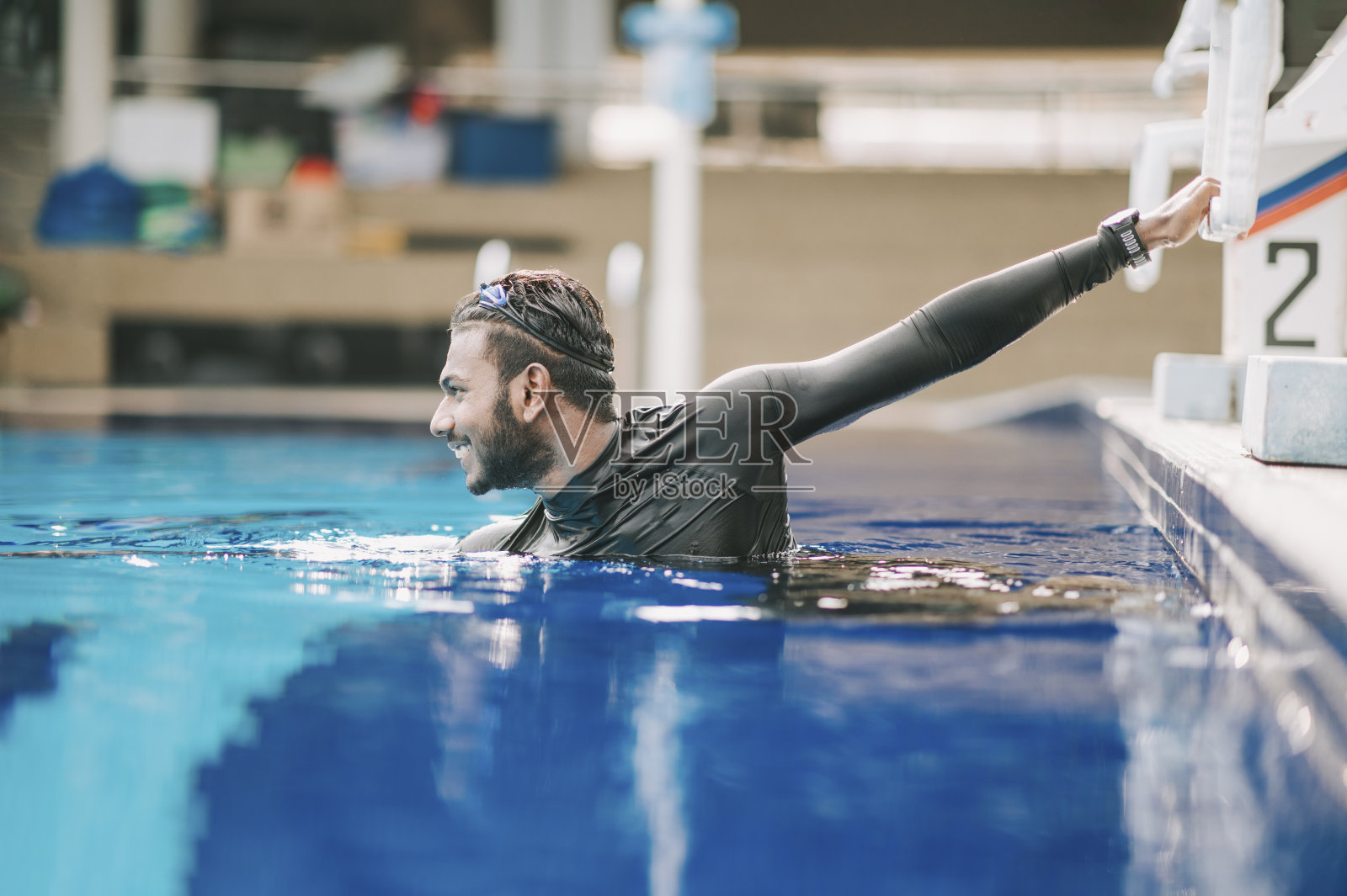 亚洲印度男子运动员游泳运动员微笑着看向公共游泳池边休息照片摄影图片