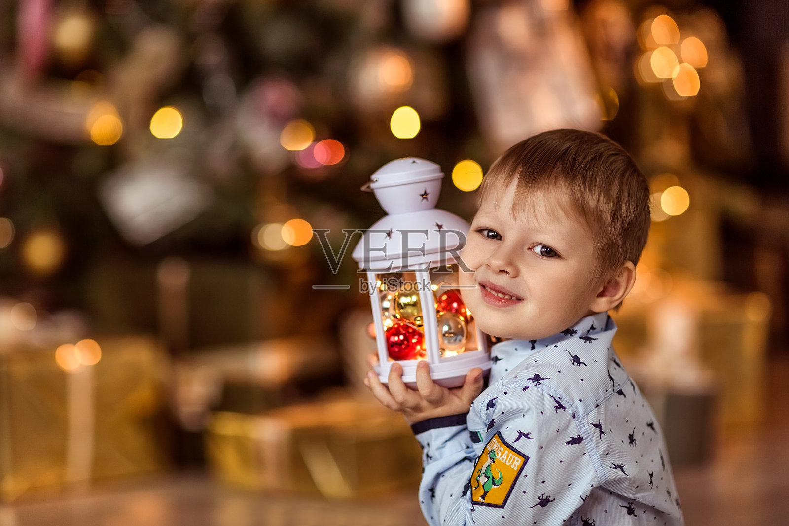 一个4-5岁的漂亮男孩坐在那里，手里拿着一个闪闪发光的手电筒。照片摄影图片