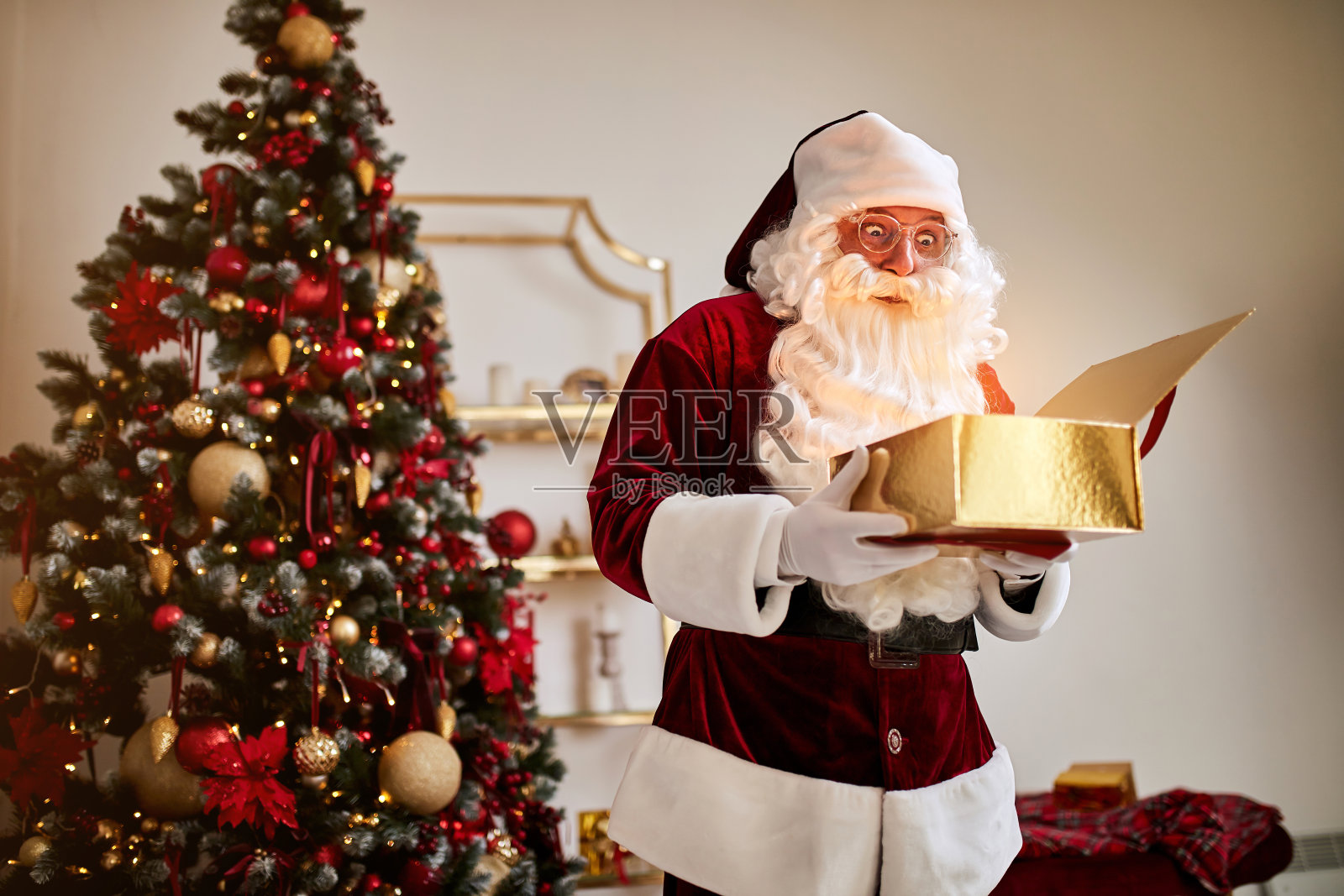 圣诞老人拿着发光的魔法礼物站在美丽的圣诞树旁，新年快乐照片摄影图片