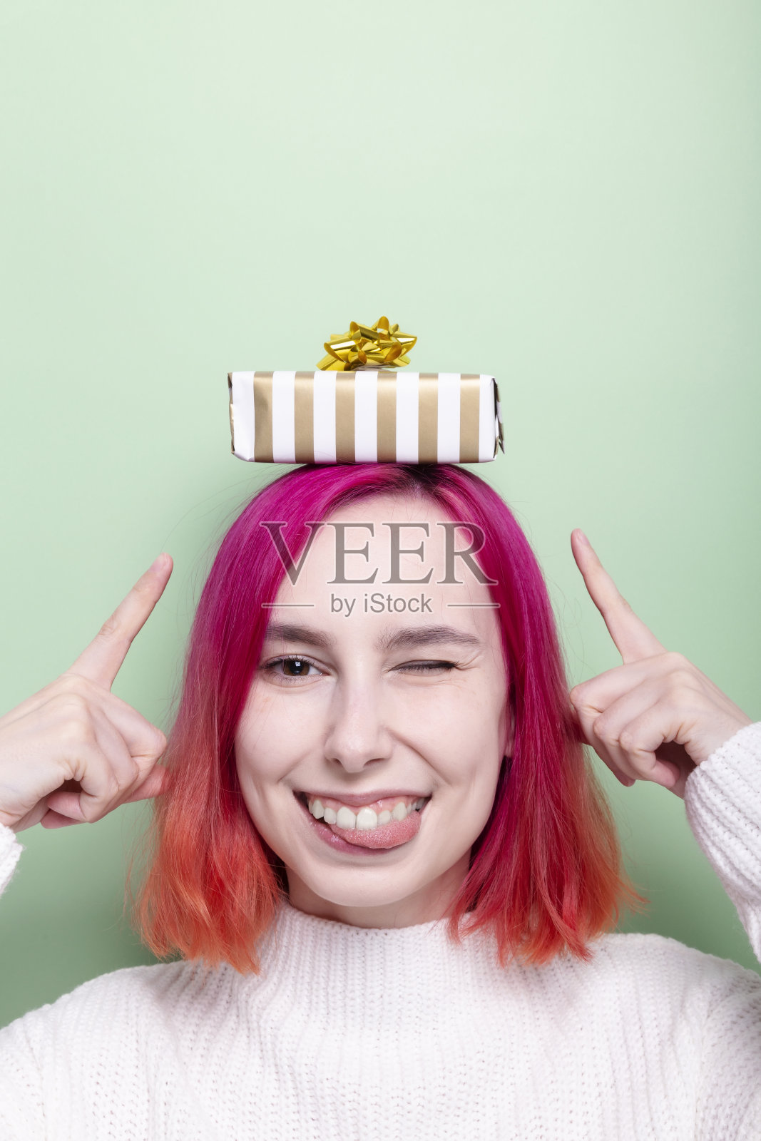 一名穿着白色毛衣，头上戴着礼品盒的女子做着鬼脸，用手指指着礼物照片摄影图片