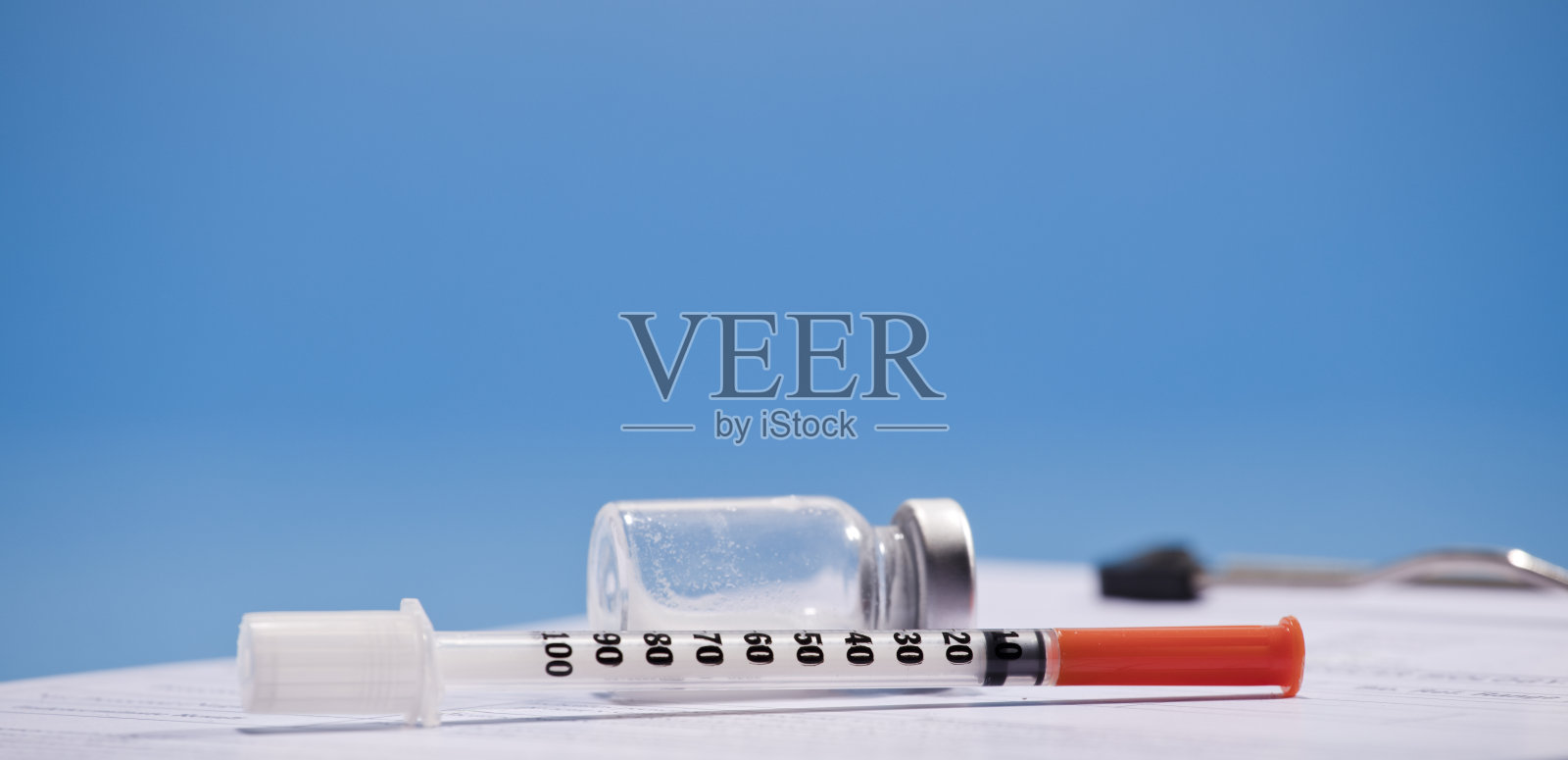 注射器和疫苗放在医院的桌子上，附有医疗报告，蓝色背景照片摄影图片