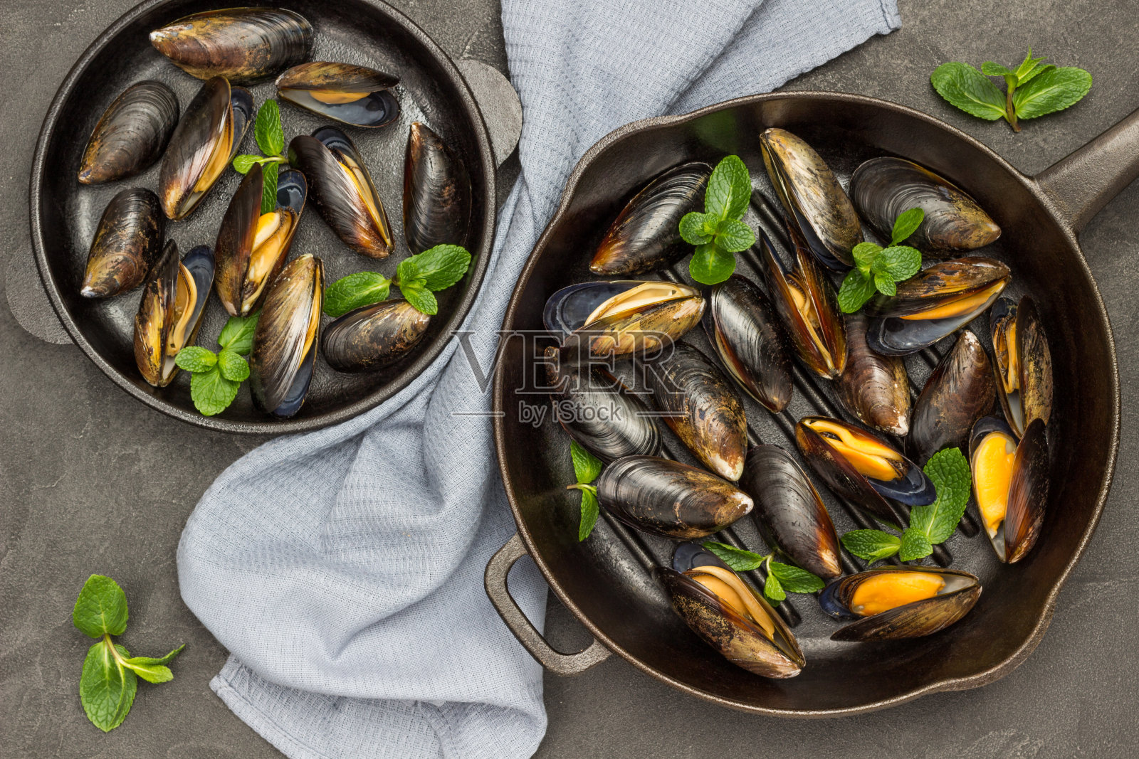 带壳生贻贝配薄荷煎锅。两只锅之间夹着灰色的餐巾。照片摄影图片