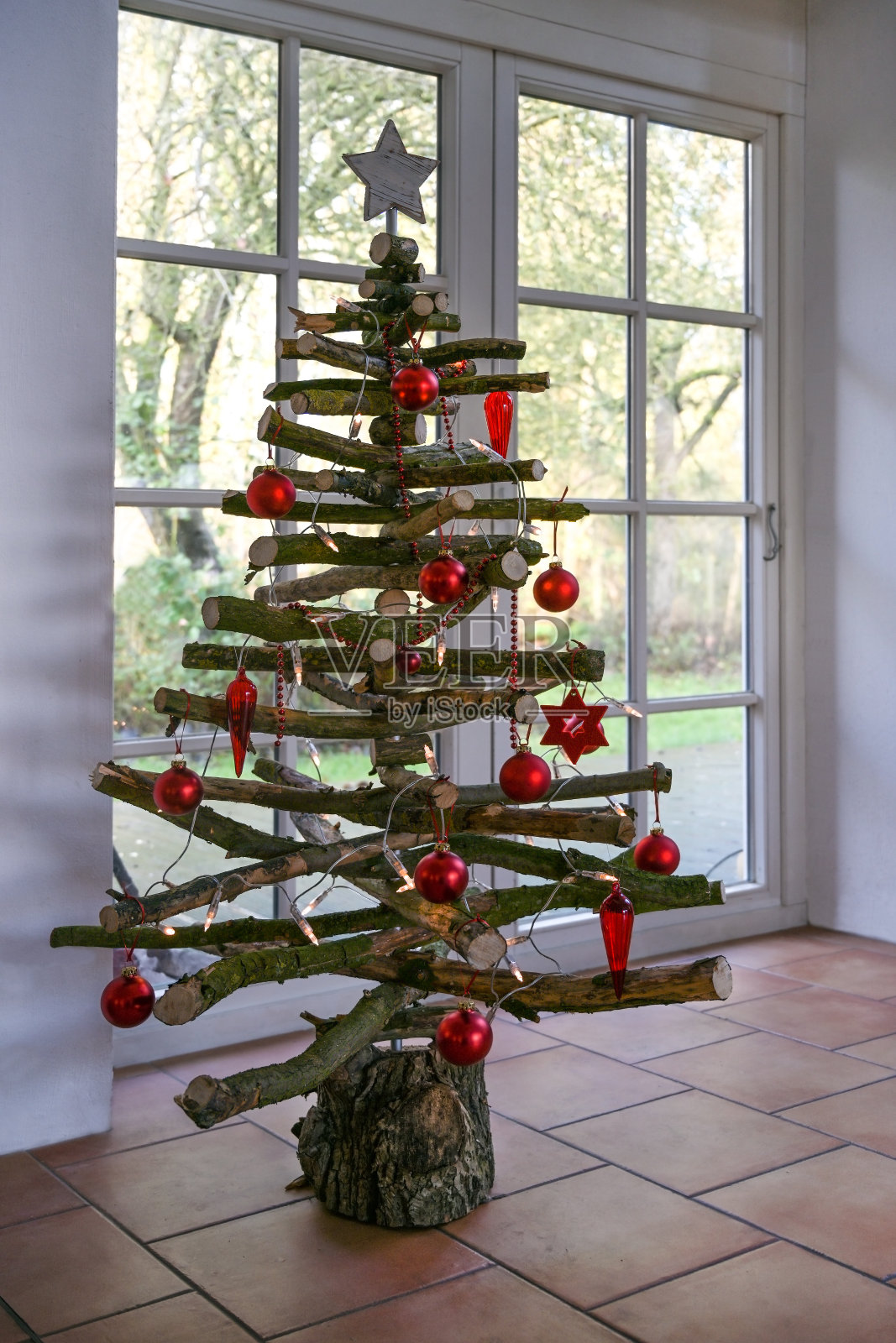 另一种圣诞树，由窗边的原始树枝制成，装饰着仙女灯和红球，为可持续和环保节日精心制作照片摄影图片