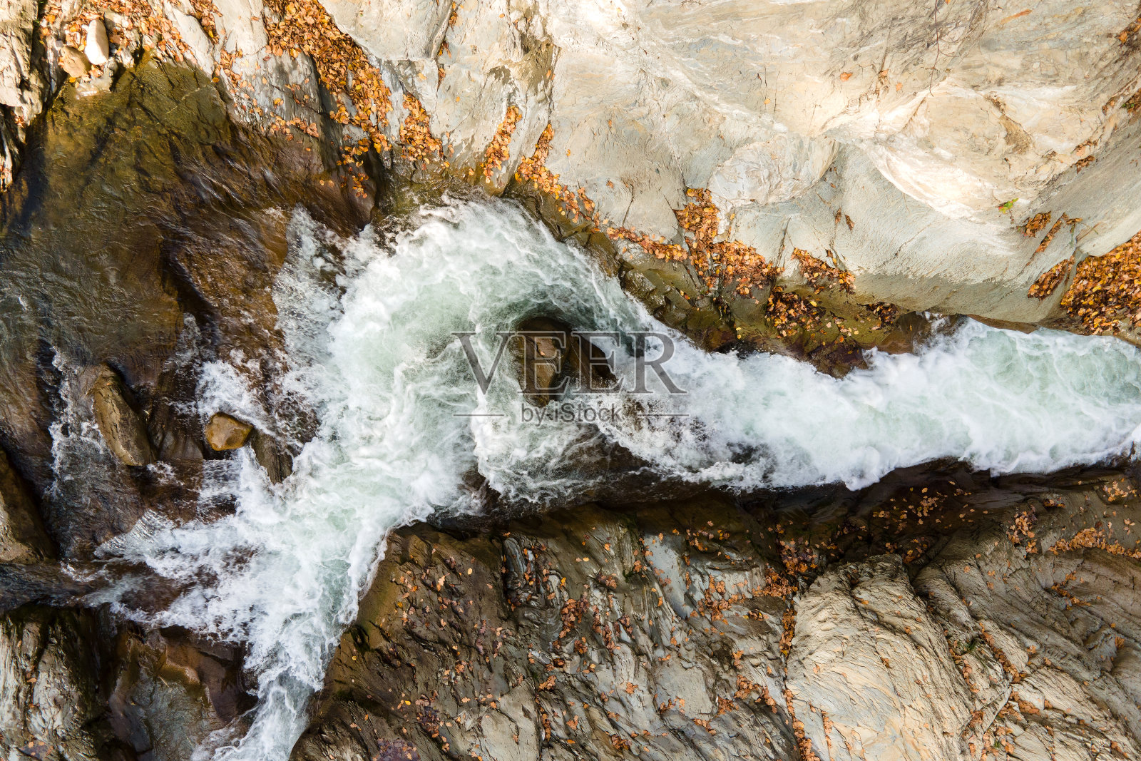 从上到下鸟瞰小山涧与快速移动的清澈的水之间的石头在秋天。照片摄影图片