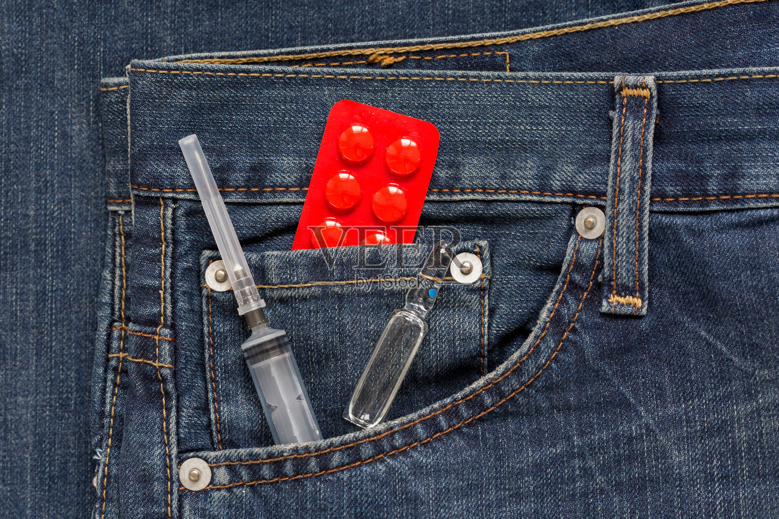 牛仔裤的侧袋里放着带壶腹和红色药丸包装的一次性注射器。药物成瘾的概念。照片摄影图片
