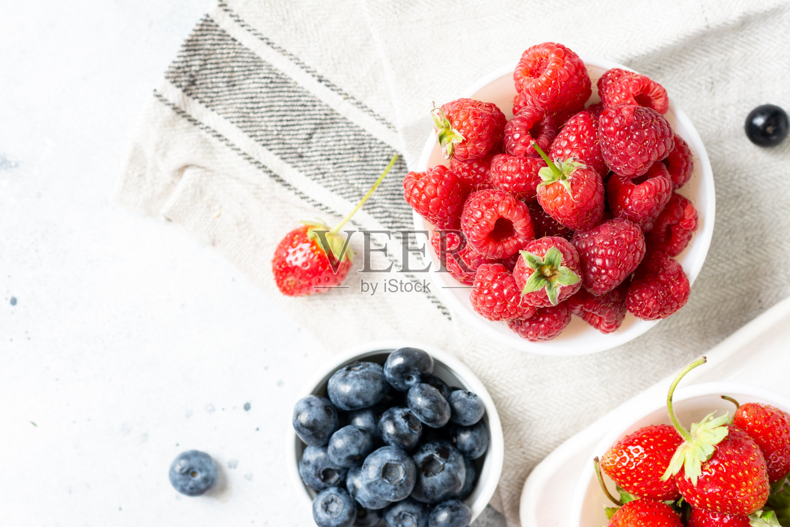 成熟的浆果。不同的浆果在白色的陶瓷碗在一个轻桌上。盘子里装着草莓、覆盆子和蓝莓照片摄影图片