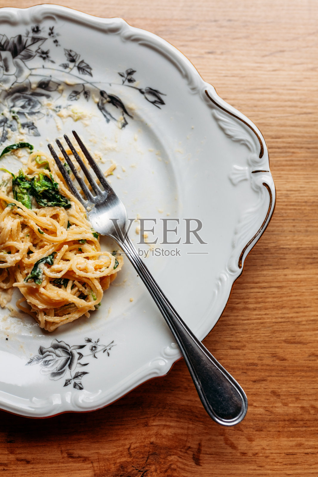 意大利面条加奶油菠菜酱和奶酪，放在凌乱的花盘上，用银叉子，在桌子上吃了一半照片摄影图片