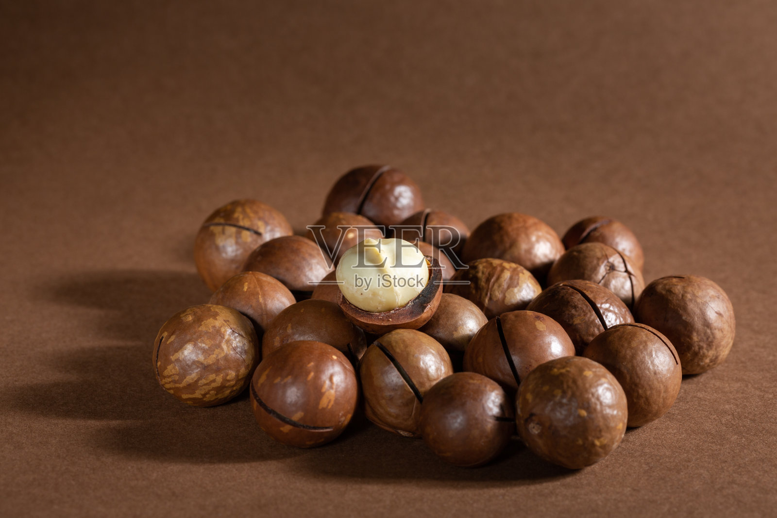 棕色背景上的一堆澳洲坚果。副本的空间。照片摄影图片